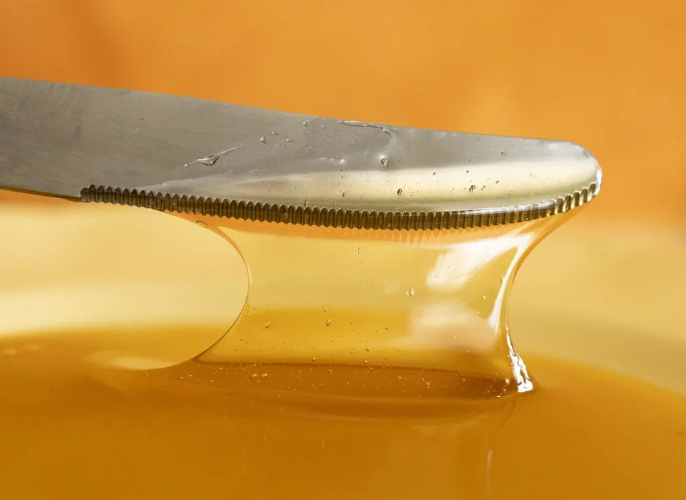 A close-up of a knife with honey dripping onto plate
