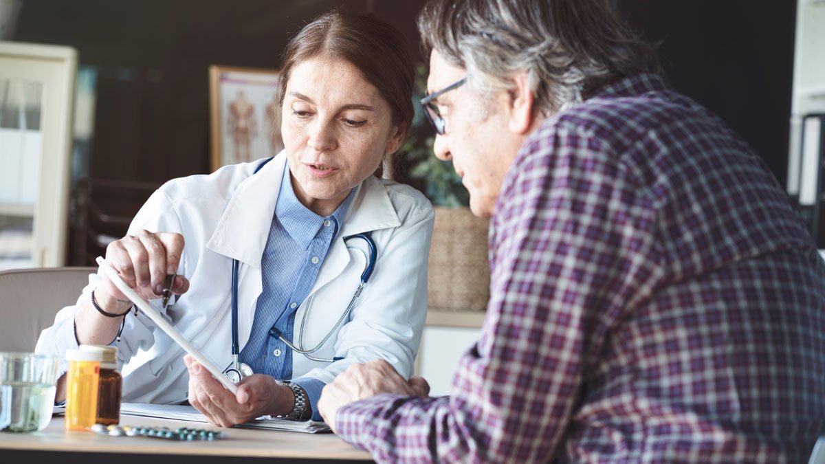 A female doctor explaining medical information to an elderly male patient in a consultation room.