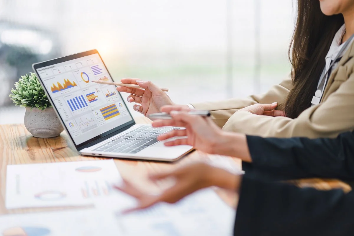 Two women reviewing data and charts on a laptop during a business meeting.