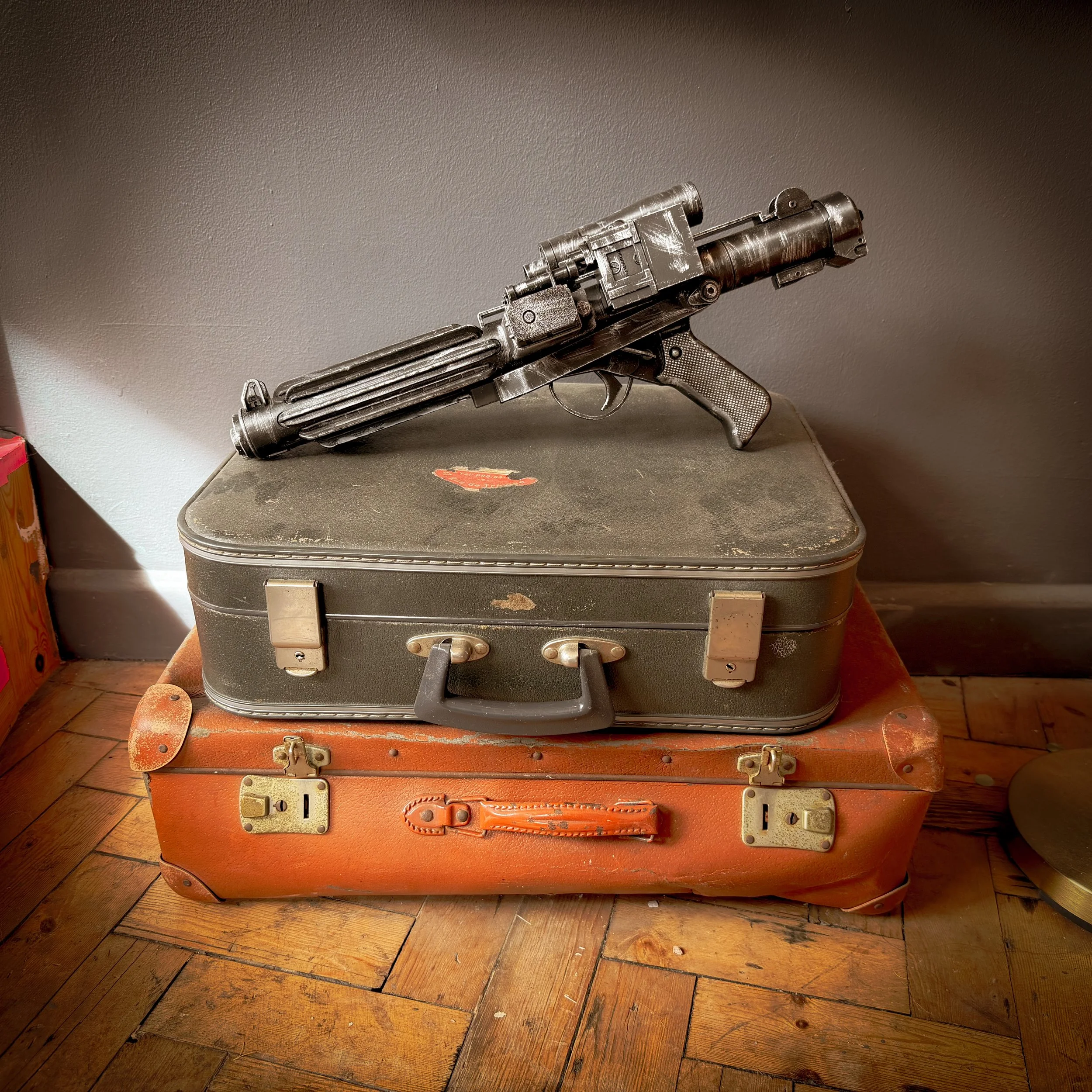 An old laser gun replica placed on top of two vintage suitcases on a hardwood floor, against a plain wall.