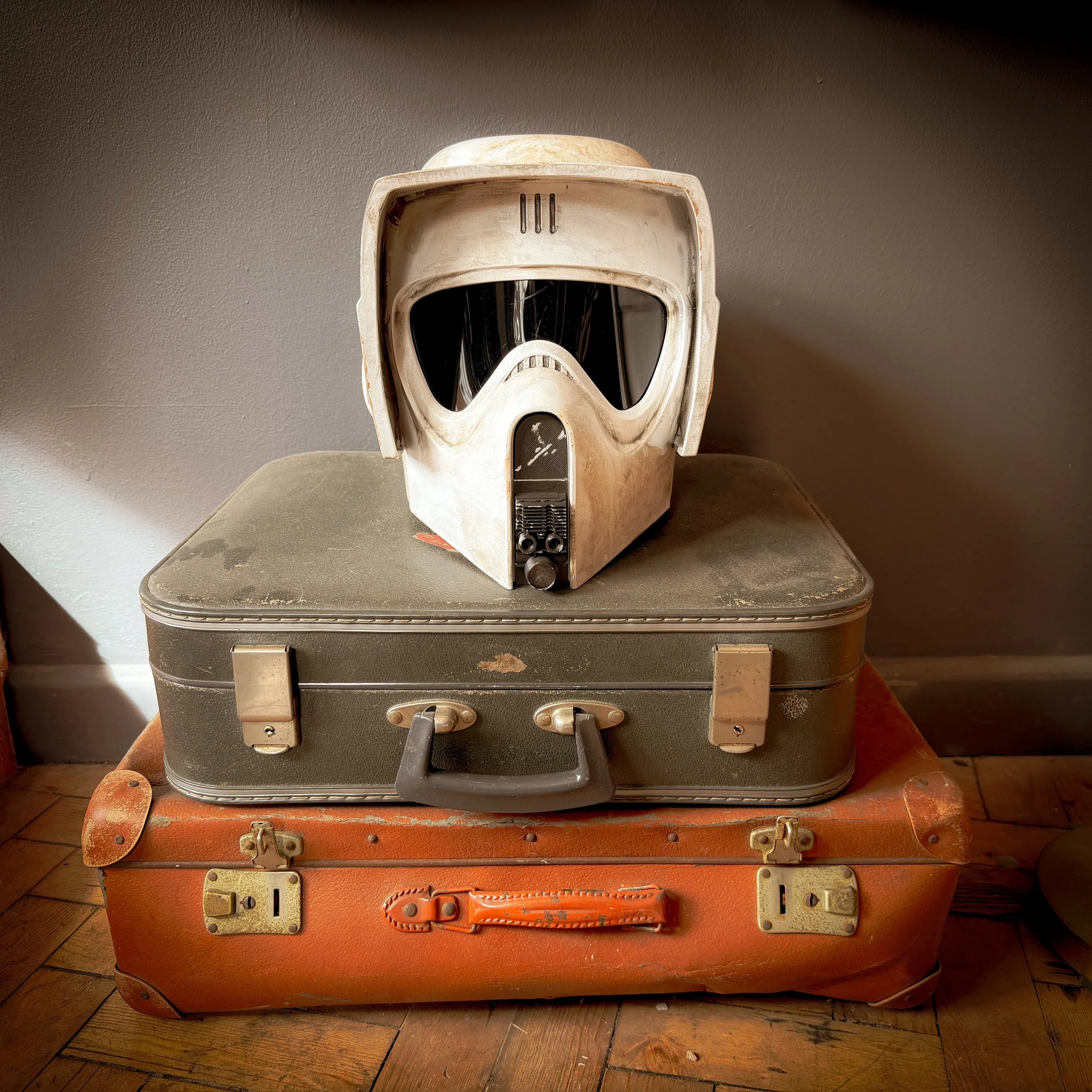 An old vintage white helmet with a black visor, placed on top of two stacked suitcases, one green and one orange.