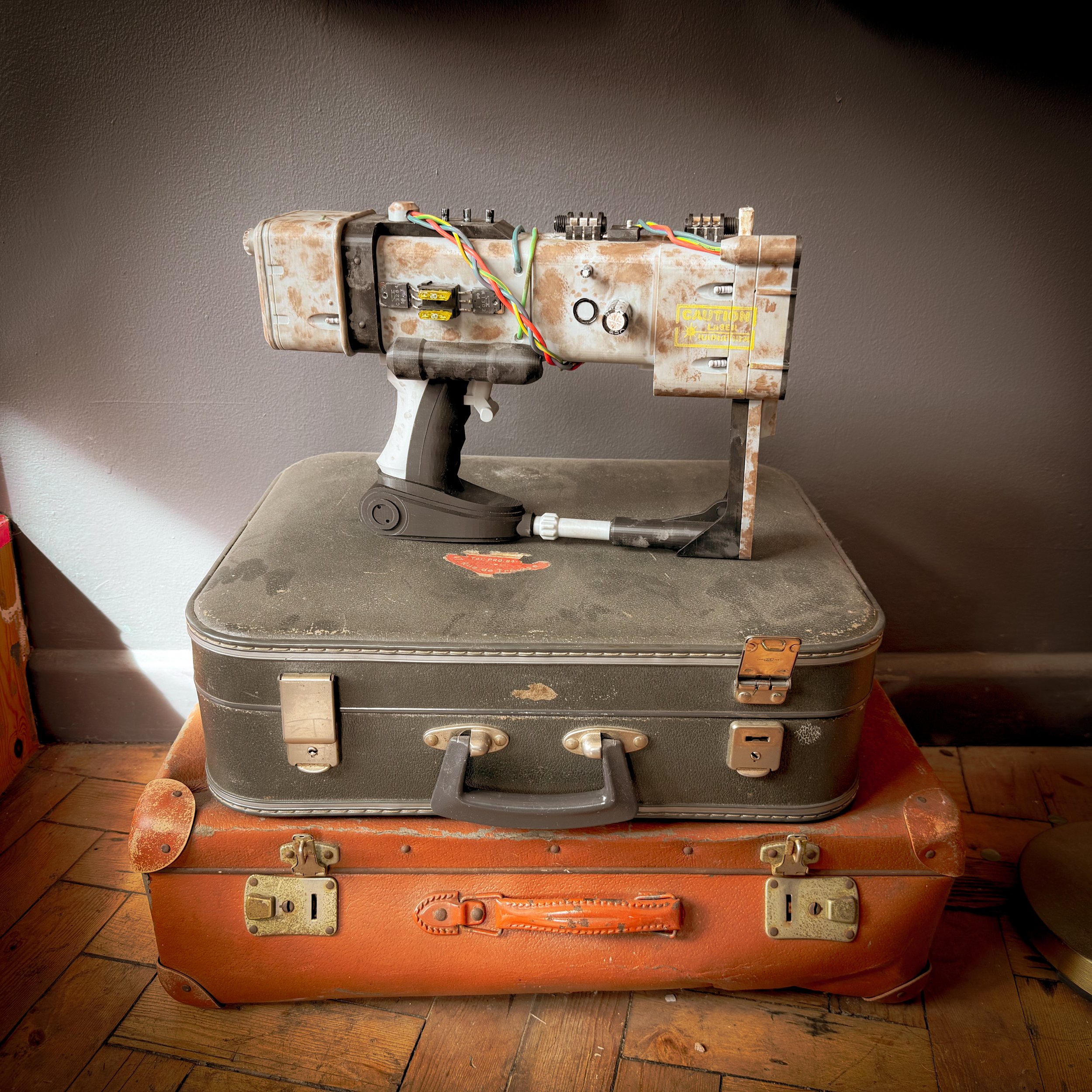A rusty, vintage laser tag gun placed on top of two stacked vintage suitcases.