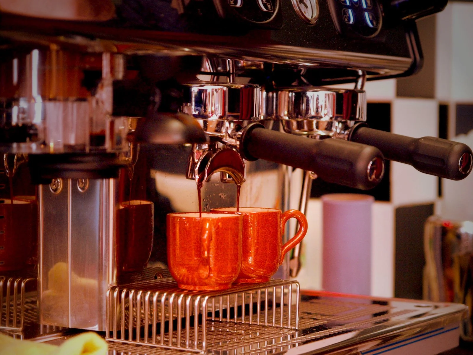 Close-up of a professional espresso machine brewing coffee into two orange mugs.