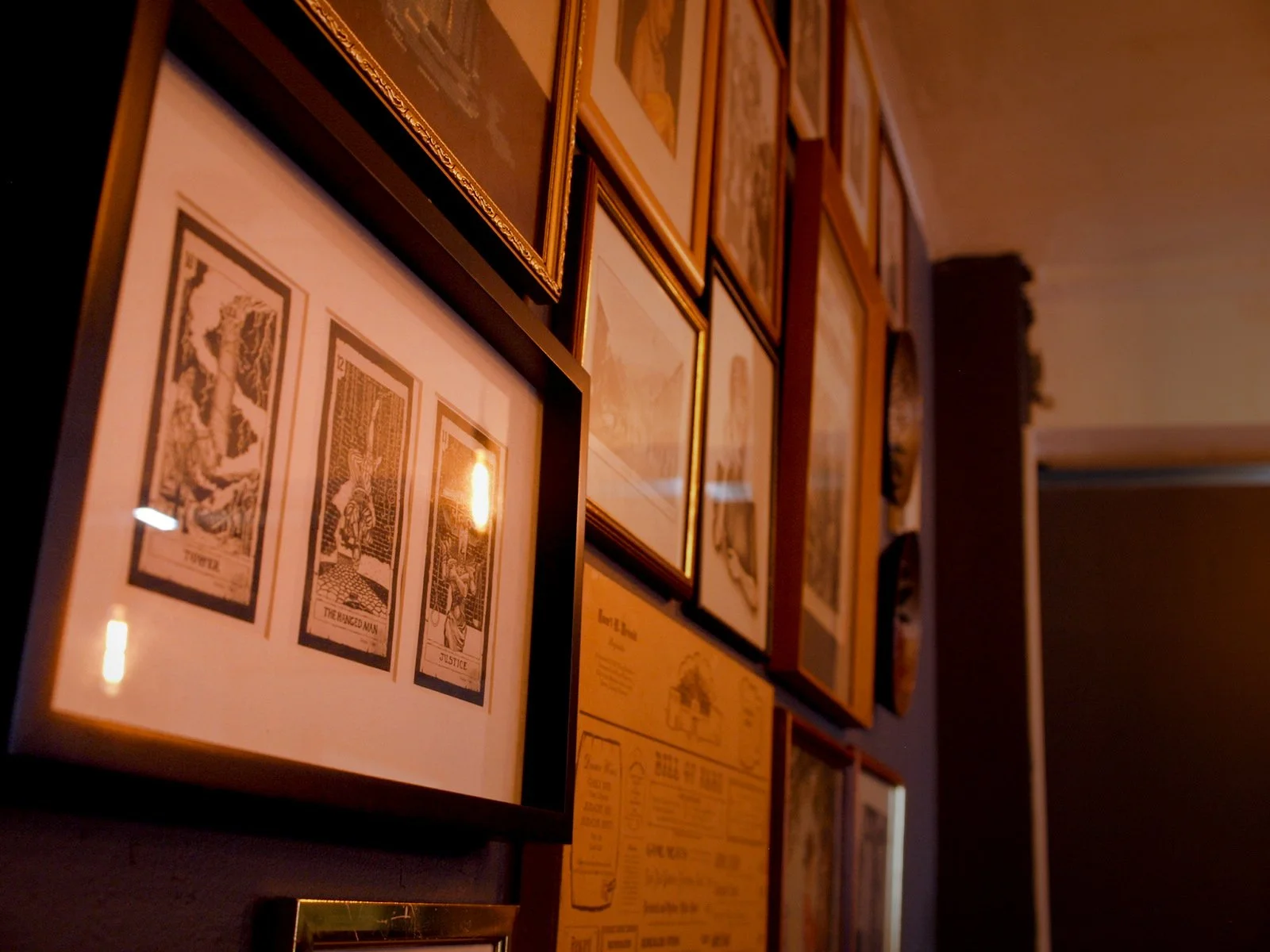 A wall decorated with multiple framed pictures and artwork, arranged in a gallery style, with warm lighting creating a cozy atmosphere.