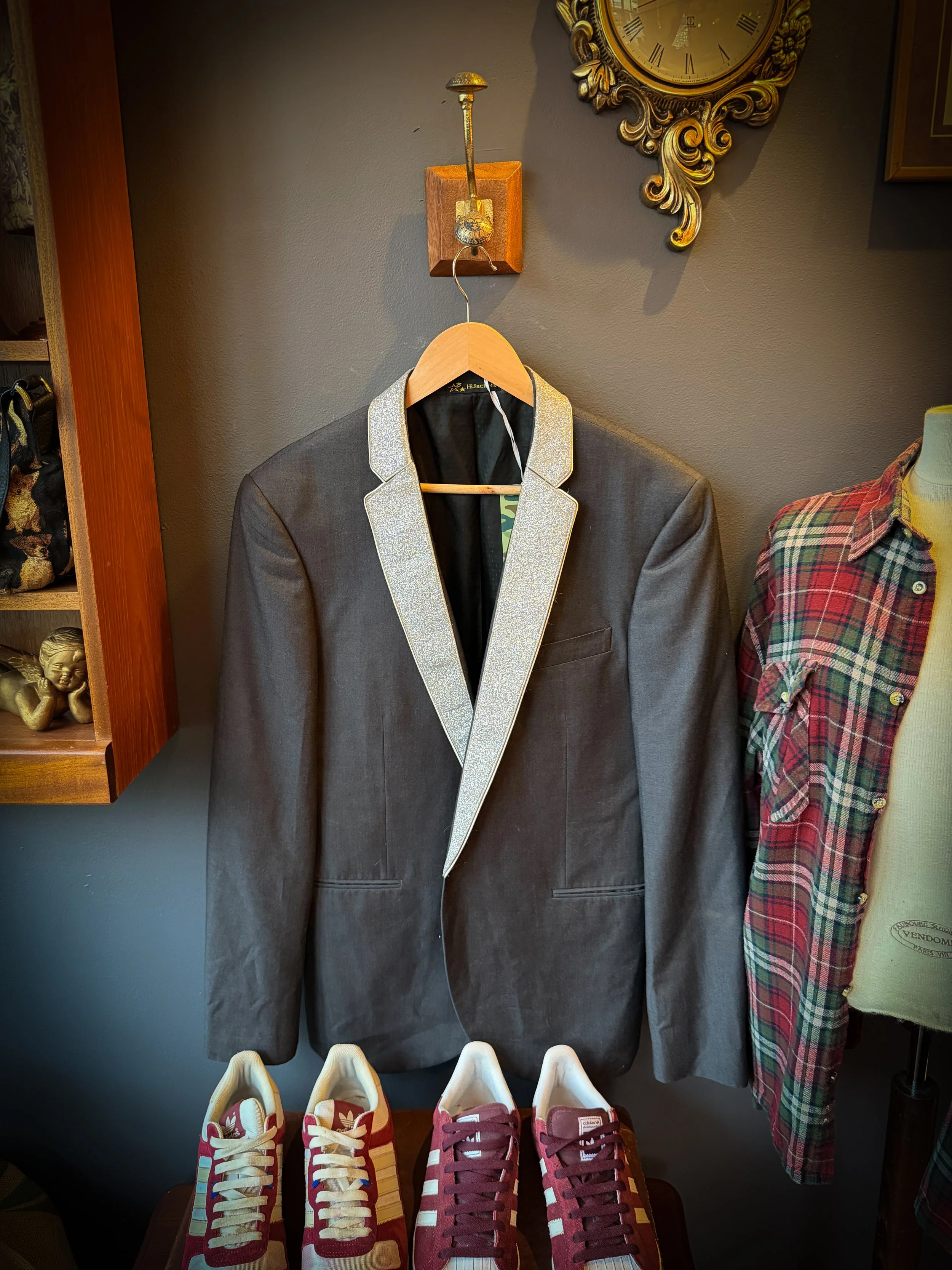 Gray tuxedo jacket with silver lapel detail hanging on a wooden hanger in a clothing store.