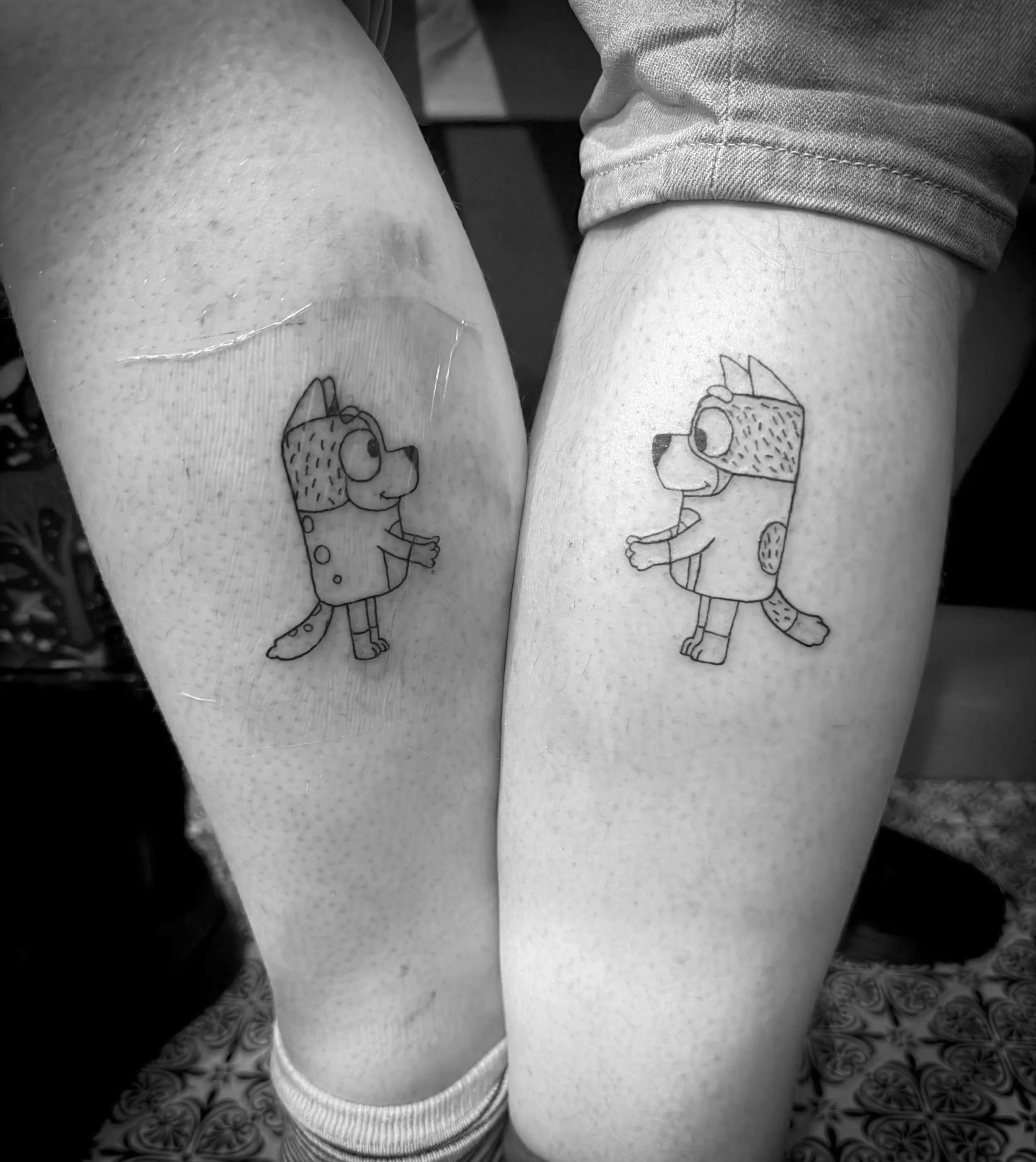 Two arms with matching cartoon dog tattoos facing each other.