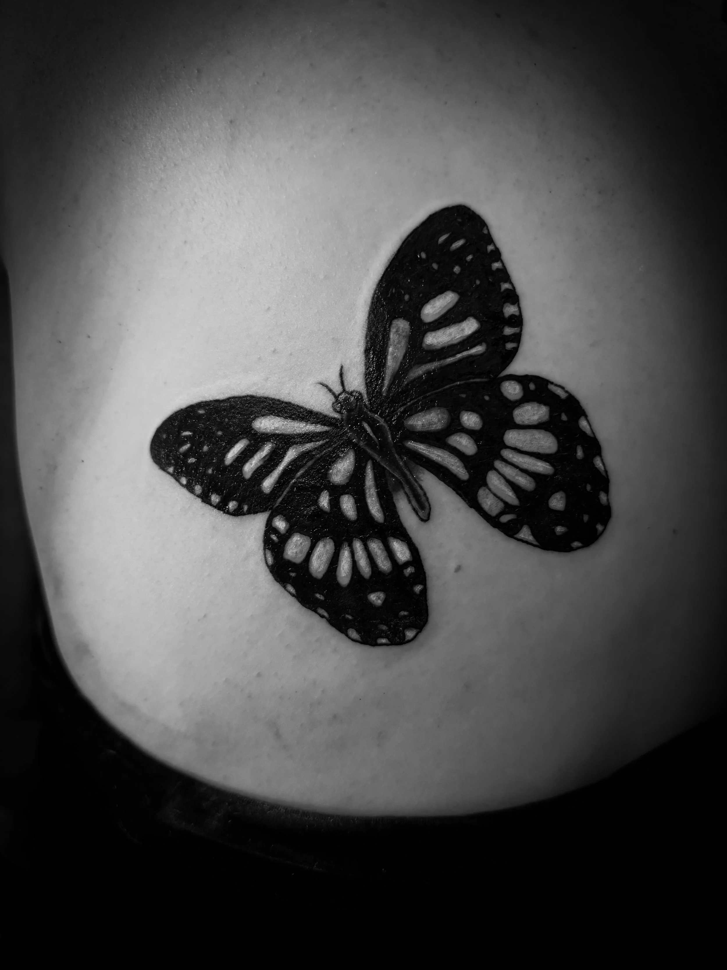 A black and white tattoo of a butterfly on skin.
