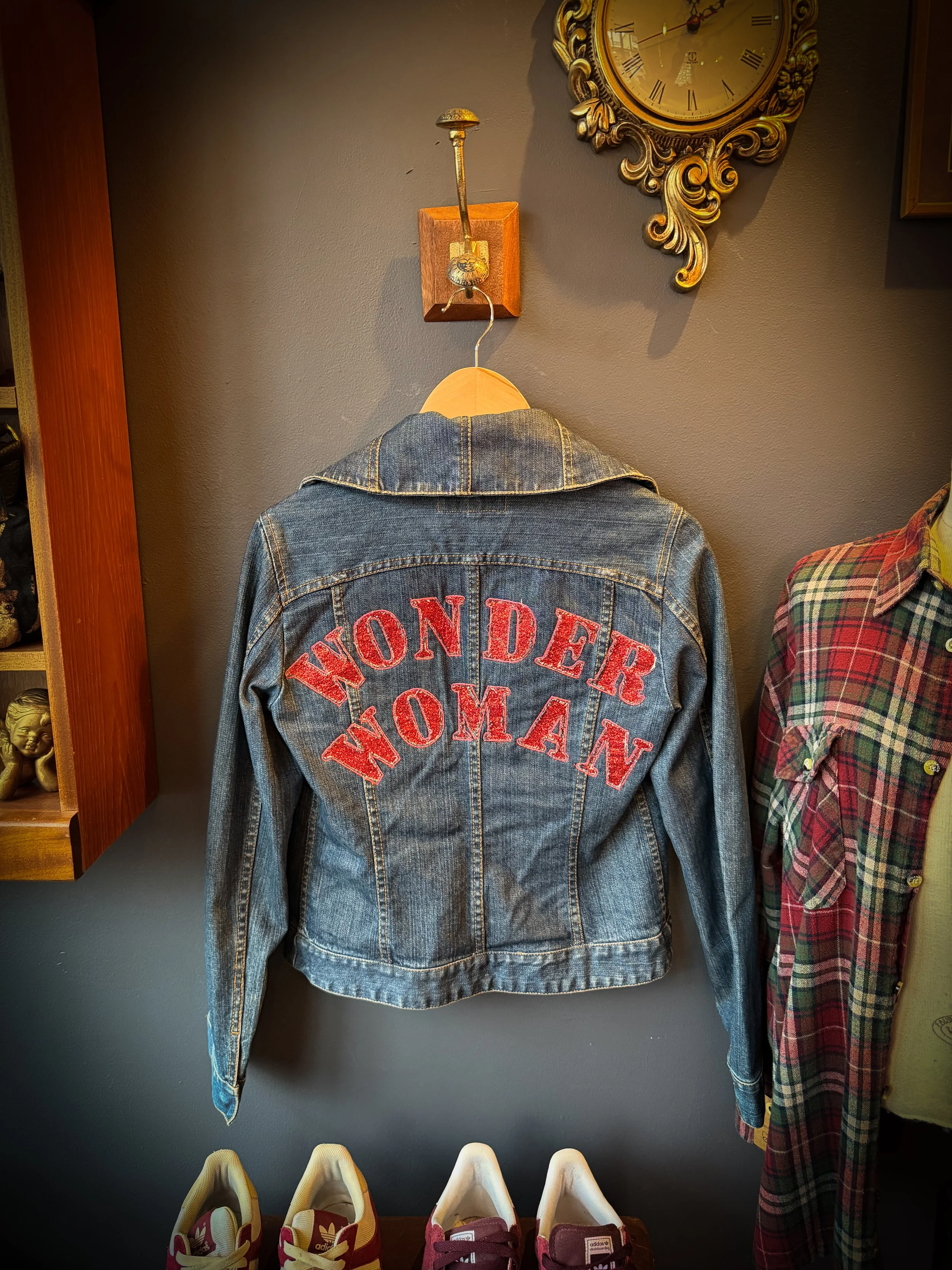 A denim jacket hanging on a wall with red embroidered text that reads "WONDER WOMAN" on the back.