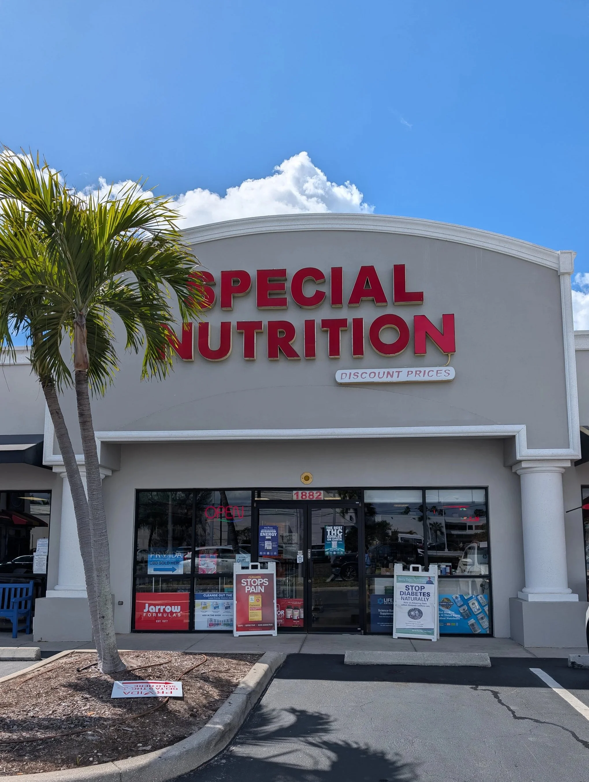 Light gray storefront with red letters spelling "Special Nutrition" above. Green palm tree on the left, two white pillars on both sides.
