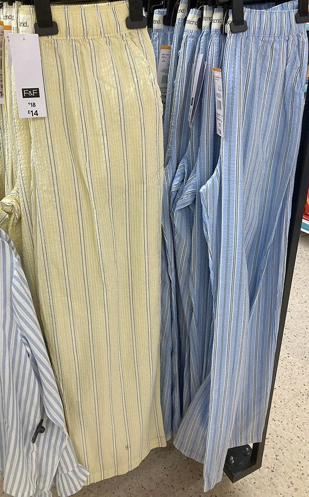 Two pairs of pyjama trousers. The left is pale yellow and the right pale blue, both with grey and white pinstripes.