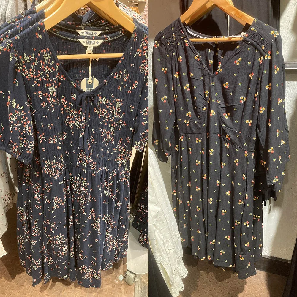 Two black dresses with floral patterns, on wooden hangers.