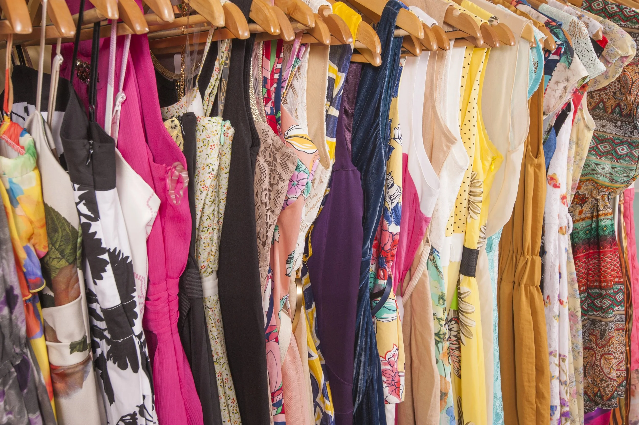 A row of dresses on wooden hangers. The dresses are all different styles and colours.