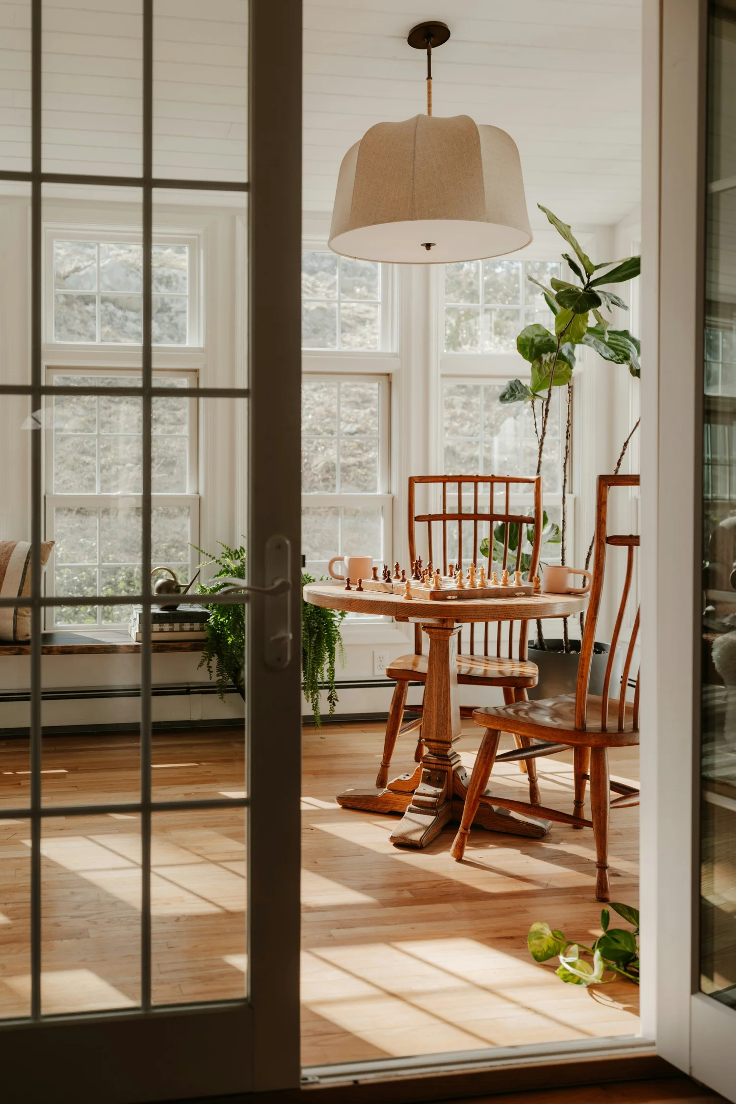 Morning light through tall windows onto a wooden table and chairs