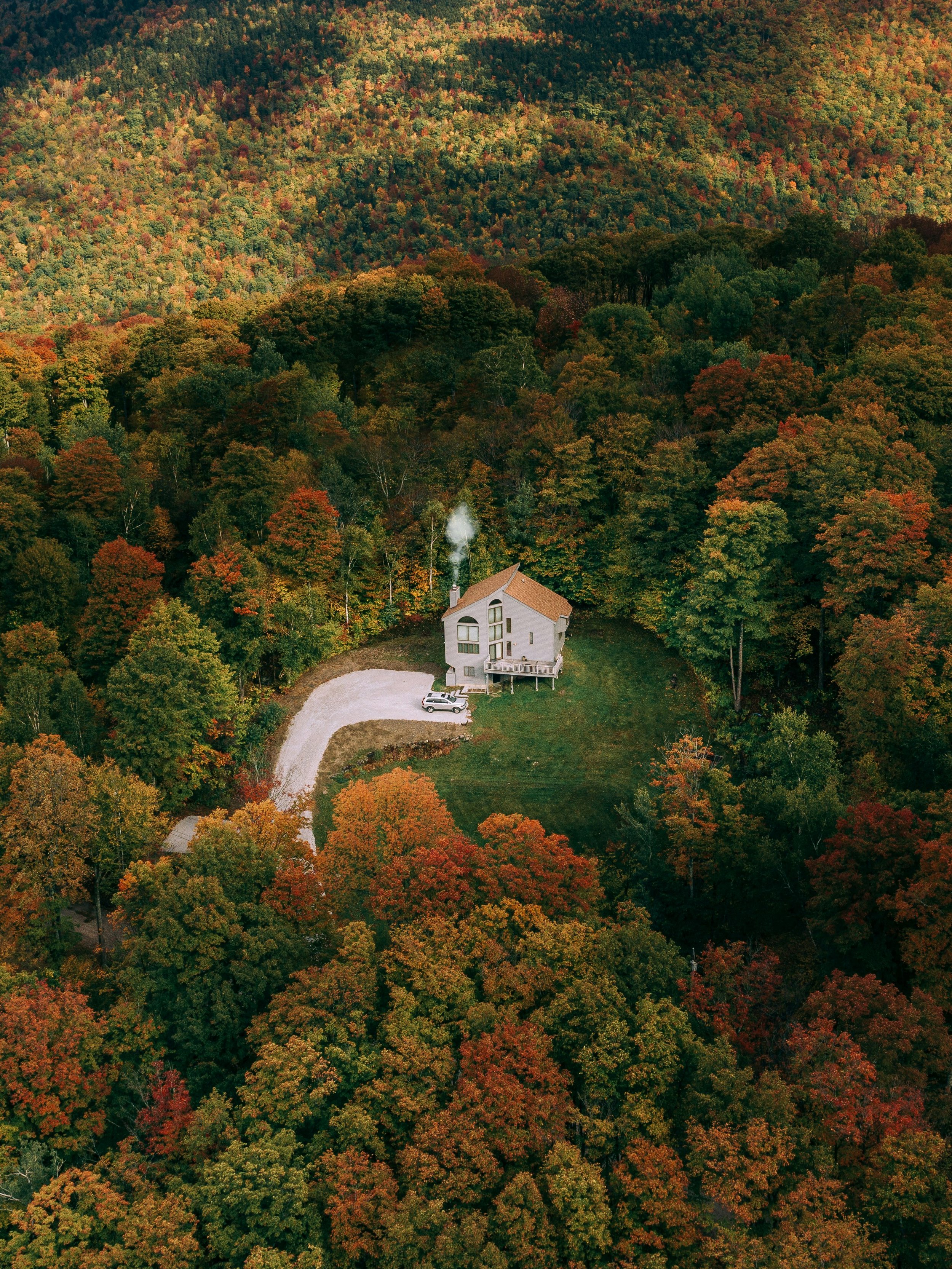 A house surrounded by a dense forest with autumn foliage, viewed from above.