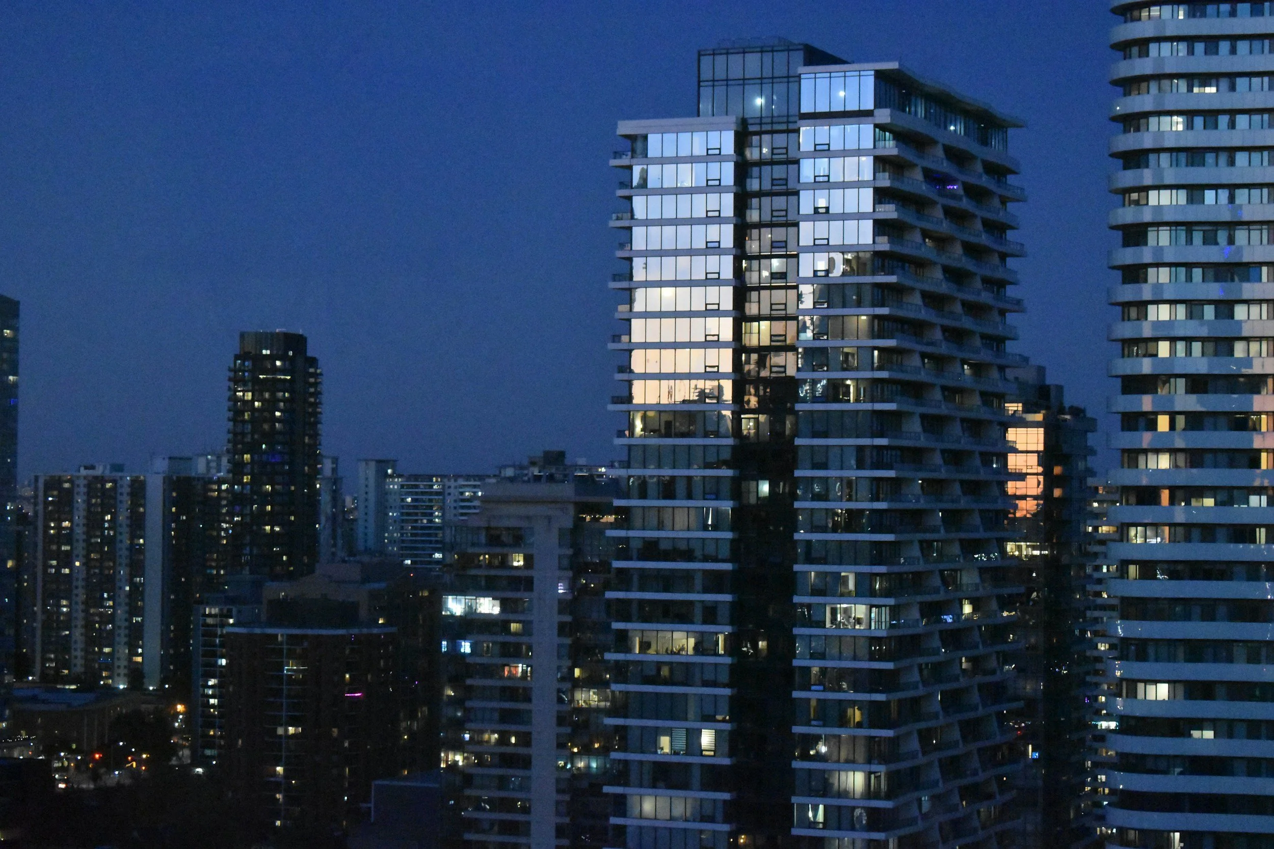 Cityscape at dusk with modern high-rise buildings and some interior lights visible.