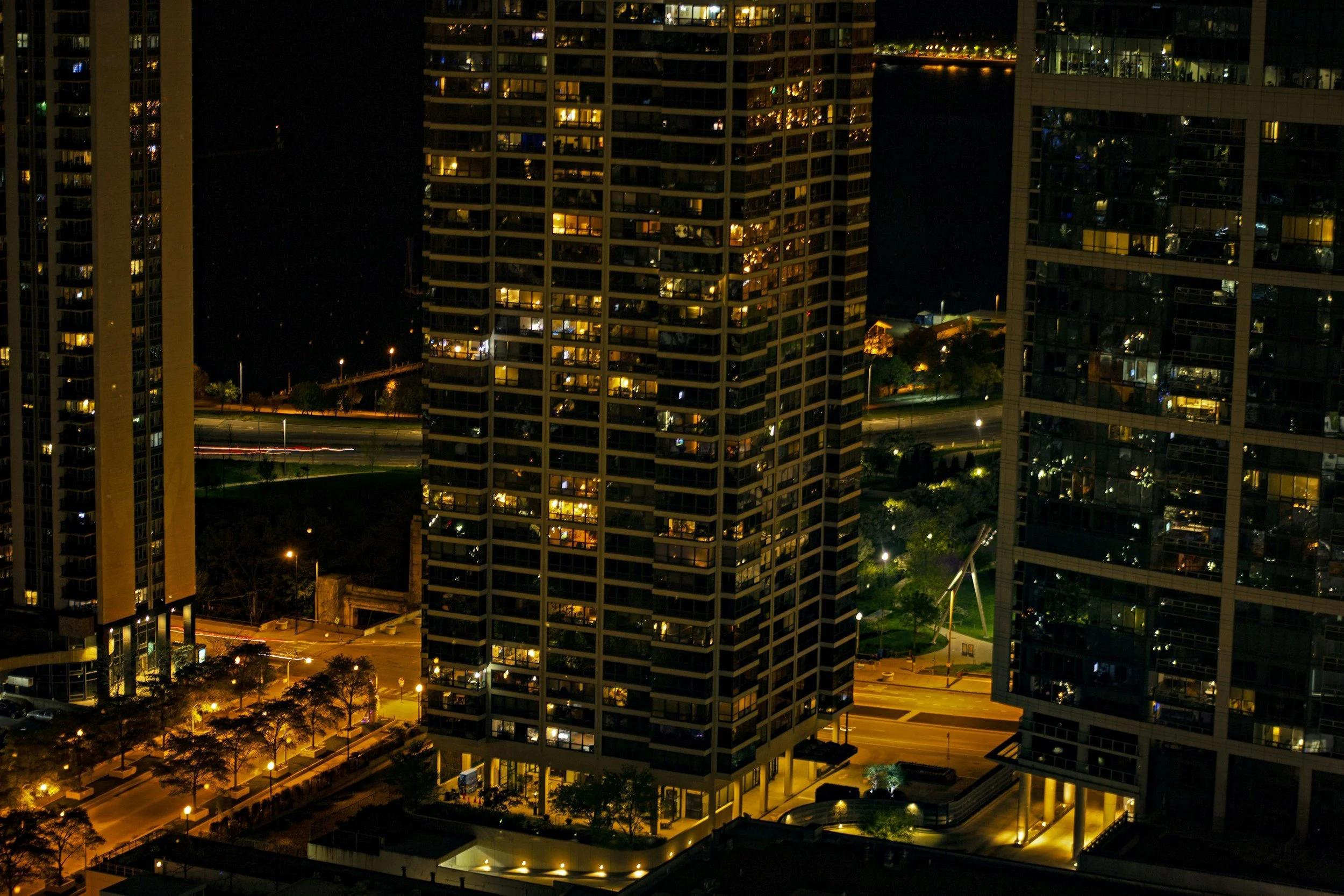 Nighttime cityscape with tall residential buildings, illuminated windows, and streetlights.