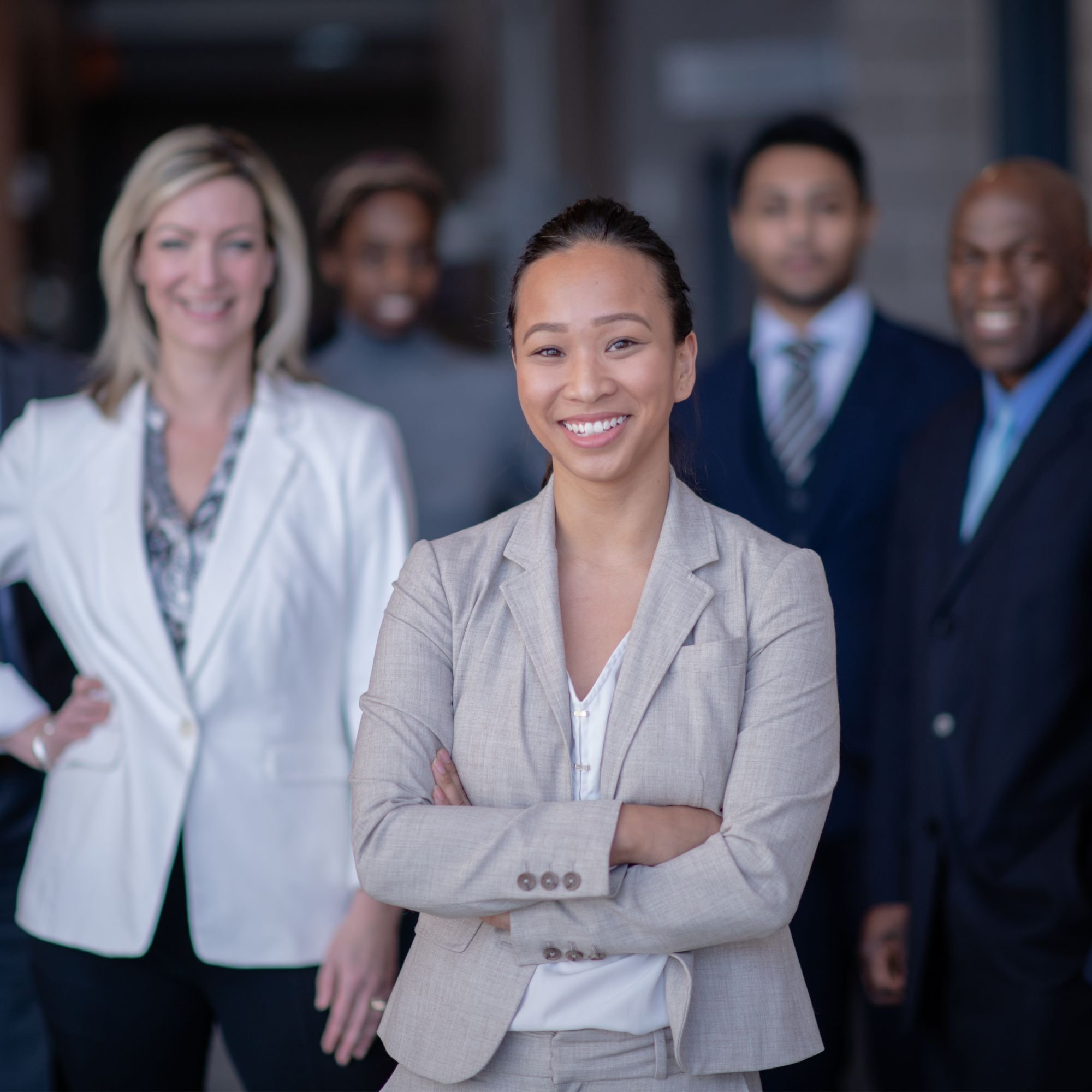 A diverse group of five professional people standing together, with a woman in a light gray blazer smiling and in the front.