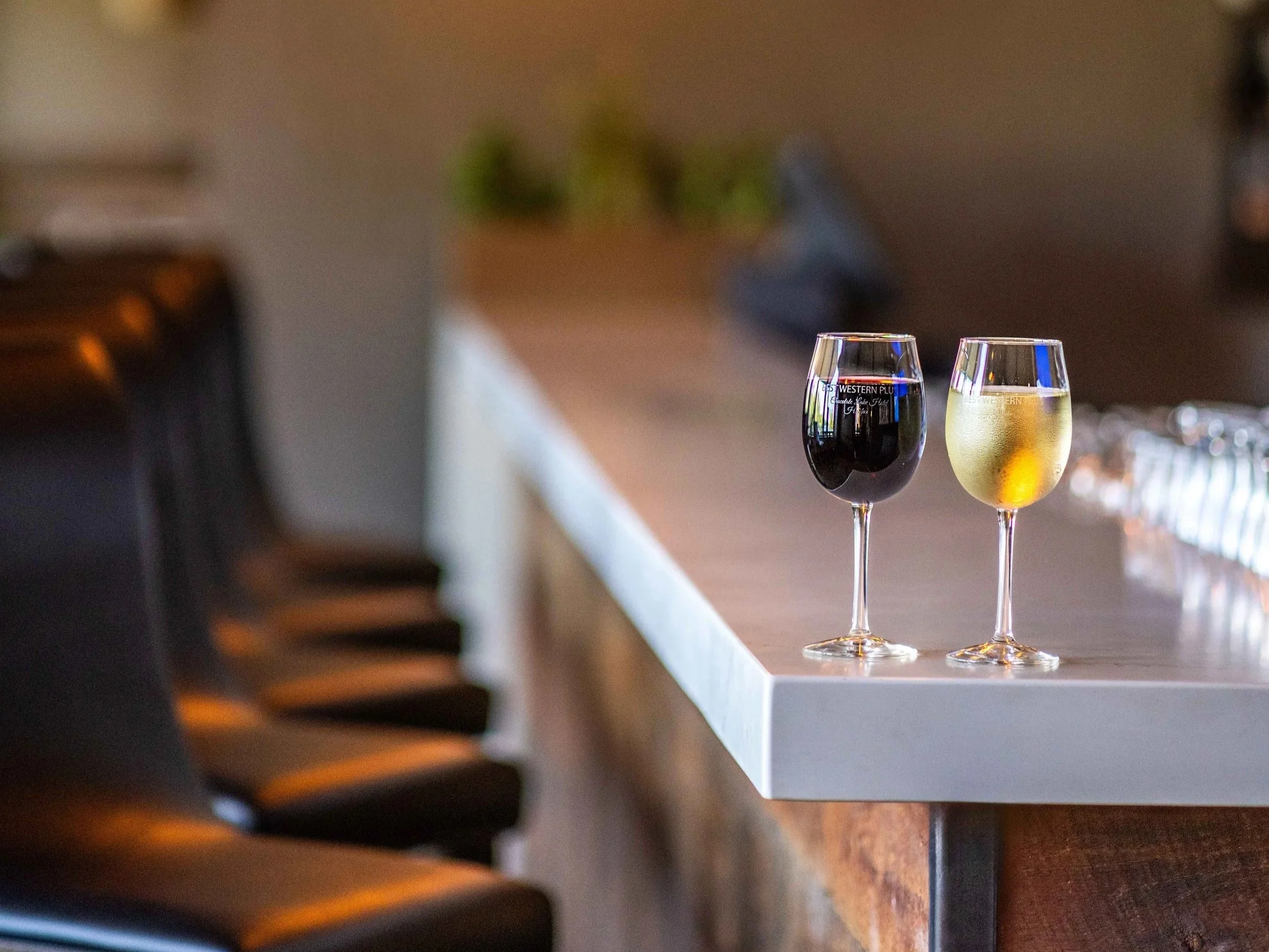 Two wine glasses, one filled with red wine and one with white wine, placed on the bar located inside Best Western Plus Chocolate Lake.