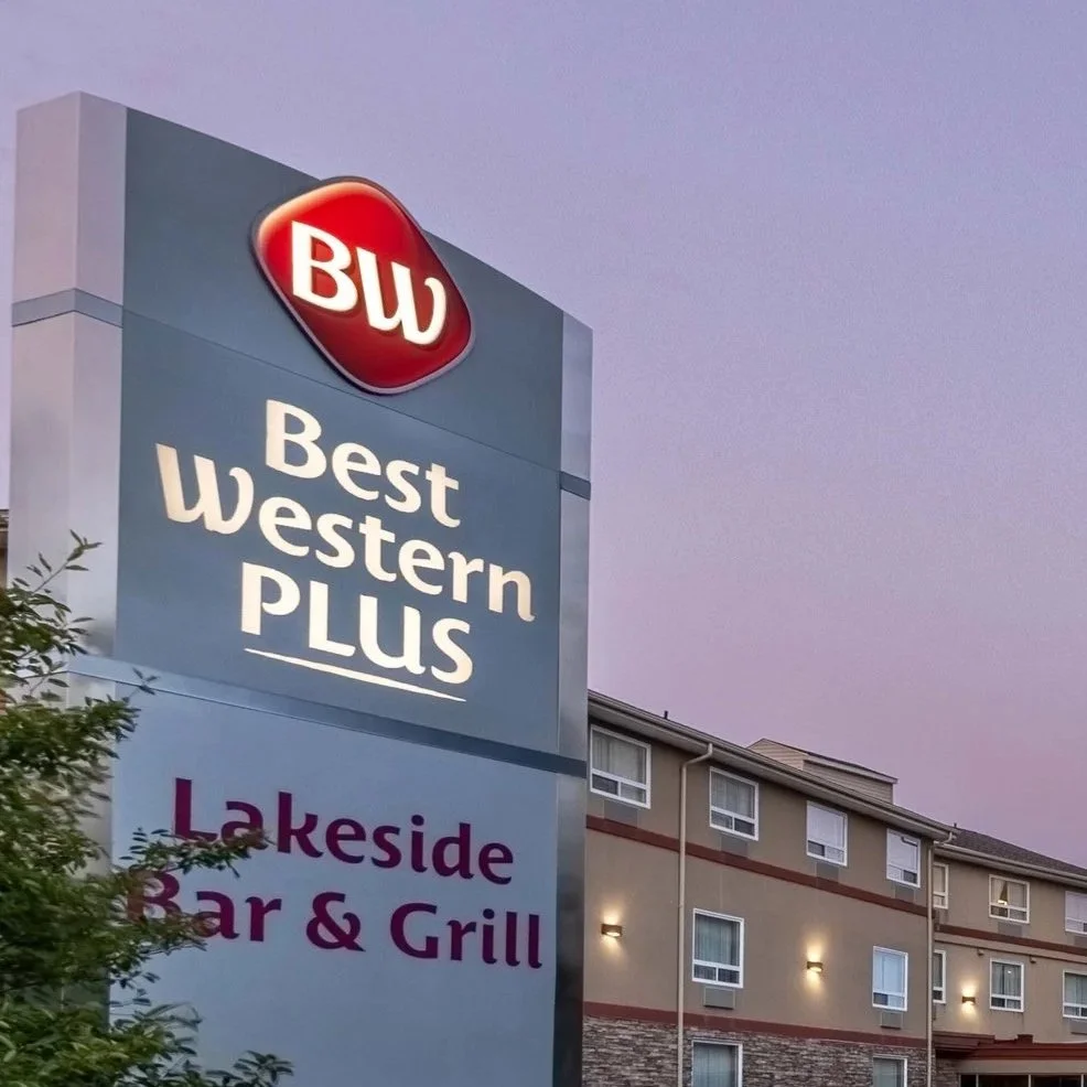 Sign for Best Western Plus Chocolate Lake hotel and  Lakeside Bar & Grill with hotel in the background, under a purple sky.