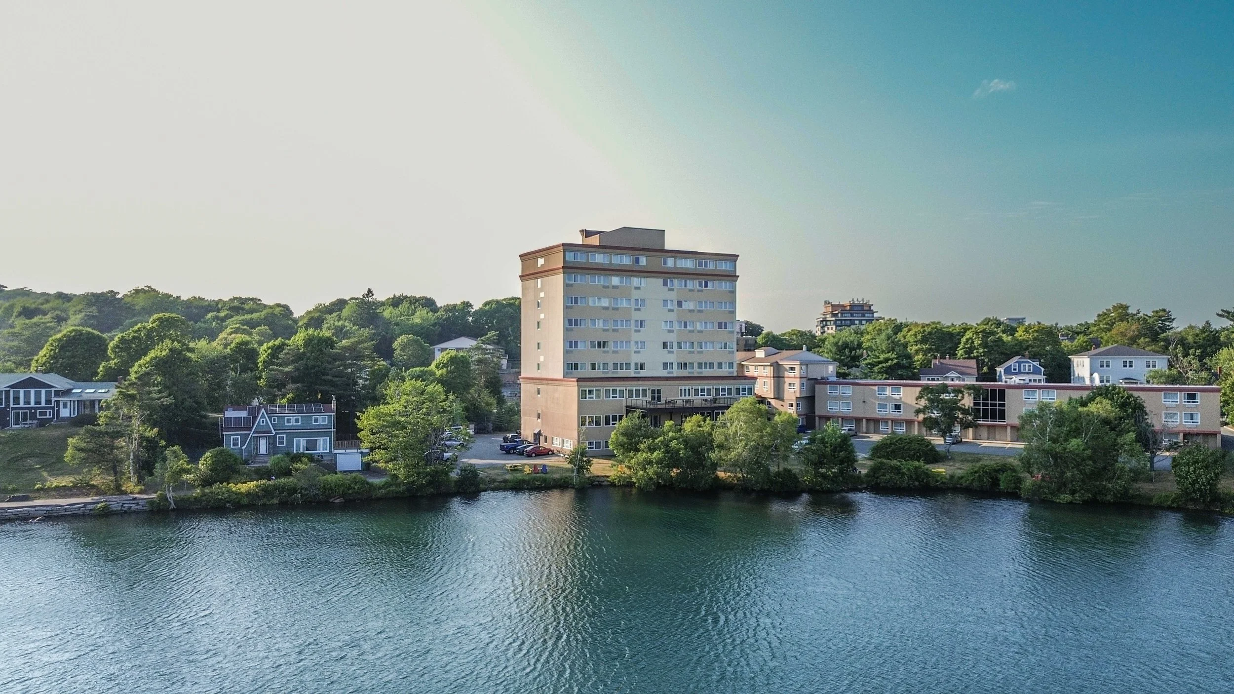 A riverfront view with Best Western Plus Chocolate Lake, and greenery in the background, under a clear blue sky.