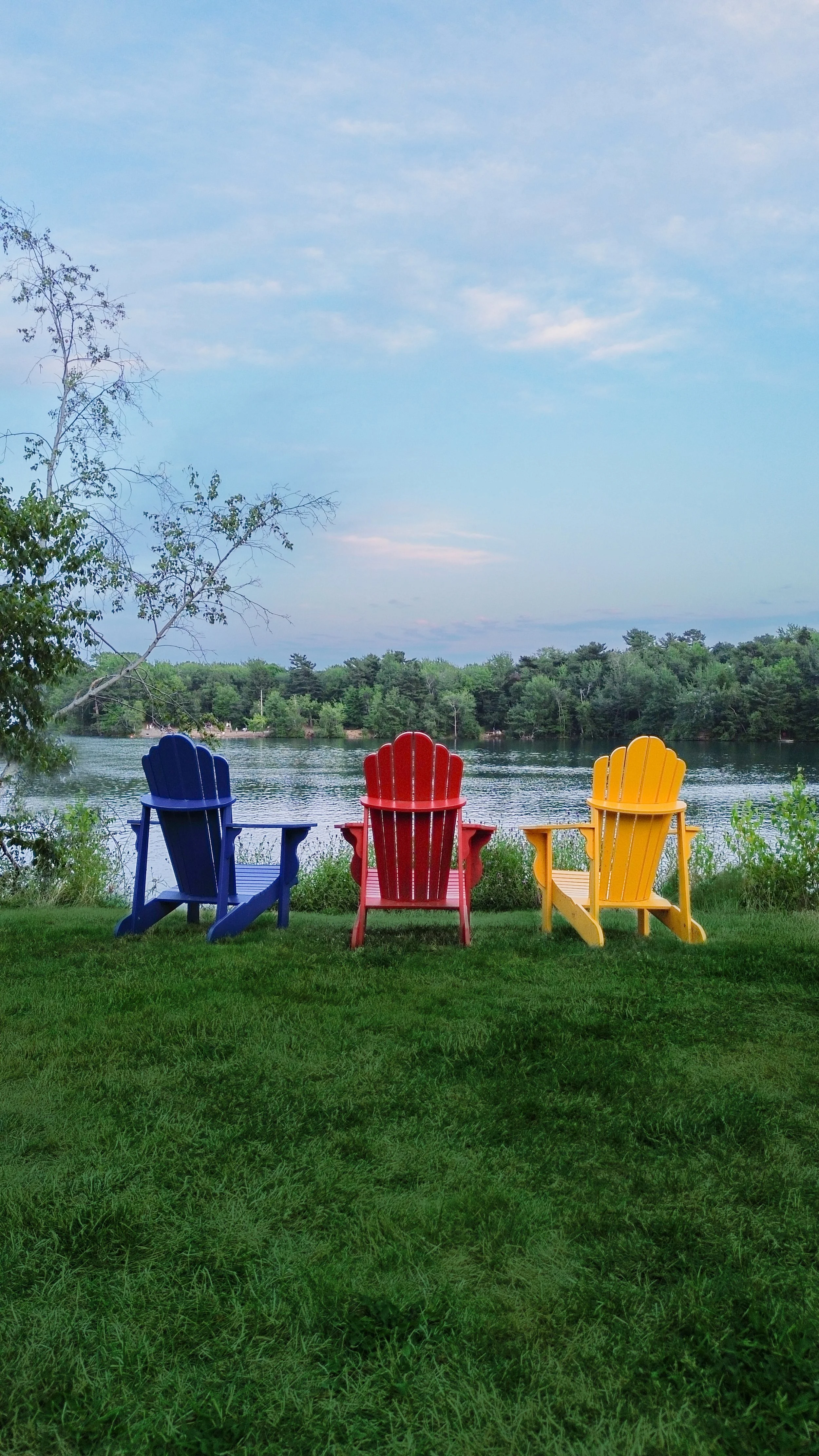 Three Adirondack chairs, painted blue, red, and yellow, in front of Chocolate Lake, located on the Best Western Plus Chocolate Lake property.