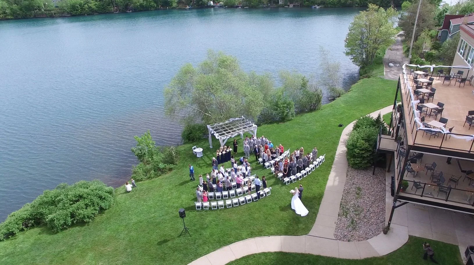 A wedding ceremony taking place outdoors at Best Western Plus Chocolate Lake, with guests gathered, seated on white chairs, and a bride standing in front of the aisle.