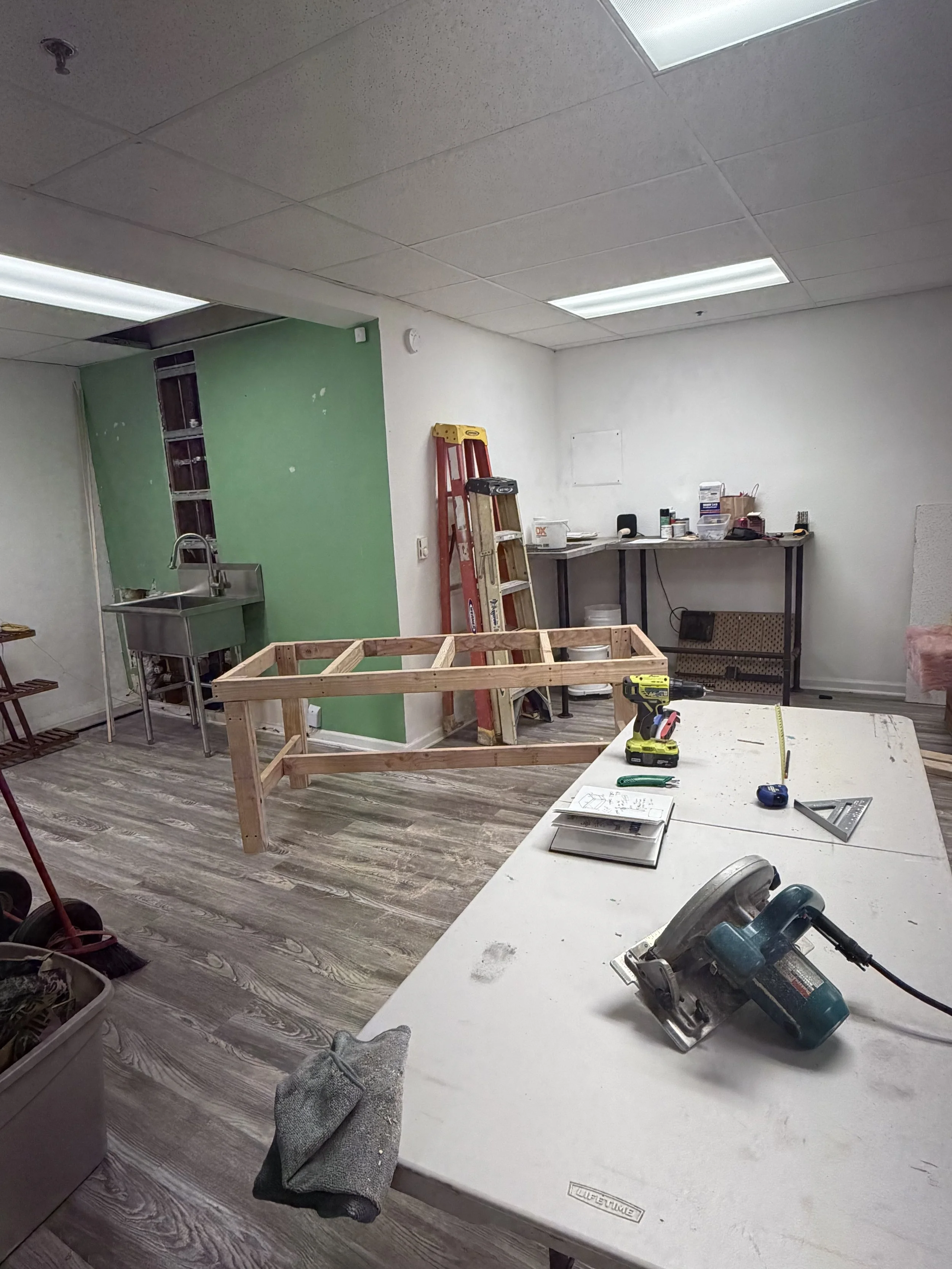 Interior of a room under renovation with construction tools on a table, a wooden frame, ladder, and construction materials.