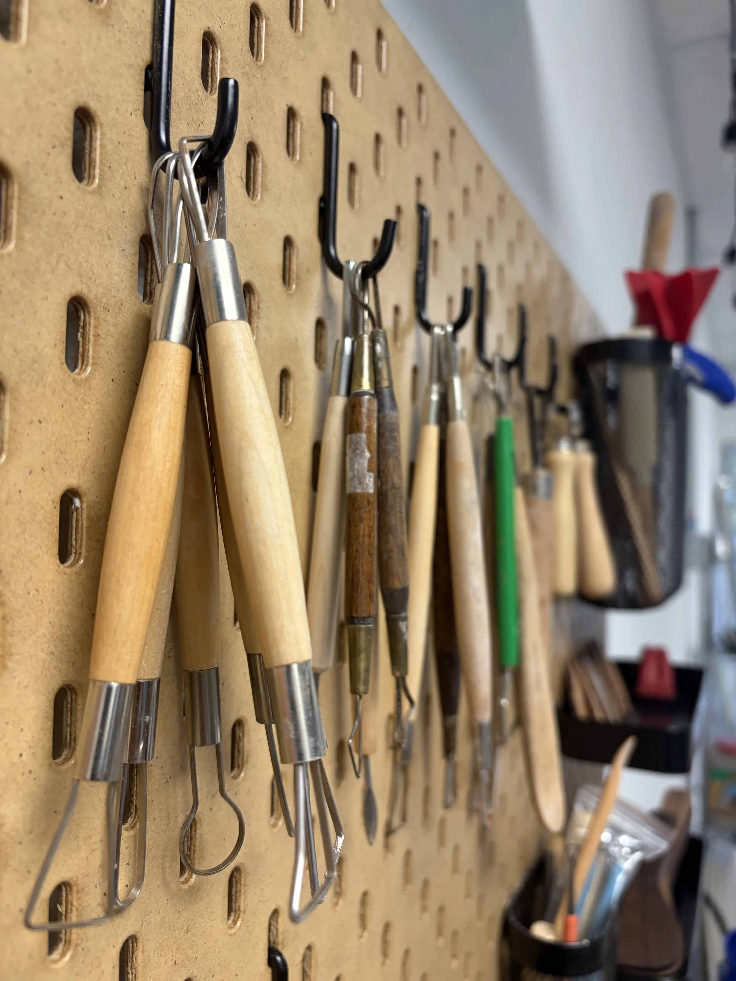A pegboard with various woodworking tools, mainly different types of carving gouges, hanging on hooks.
