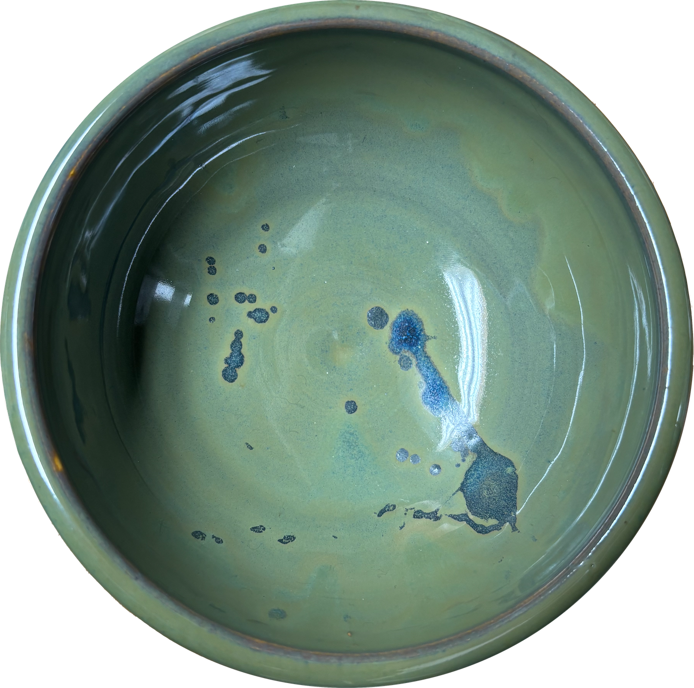 A round green ceramic bowl with a shiny, glazed interior showing blue and black paint splatters and streaks.