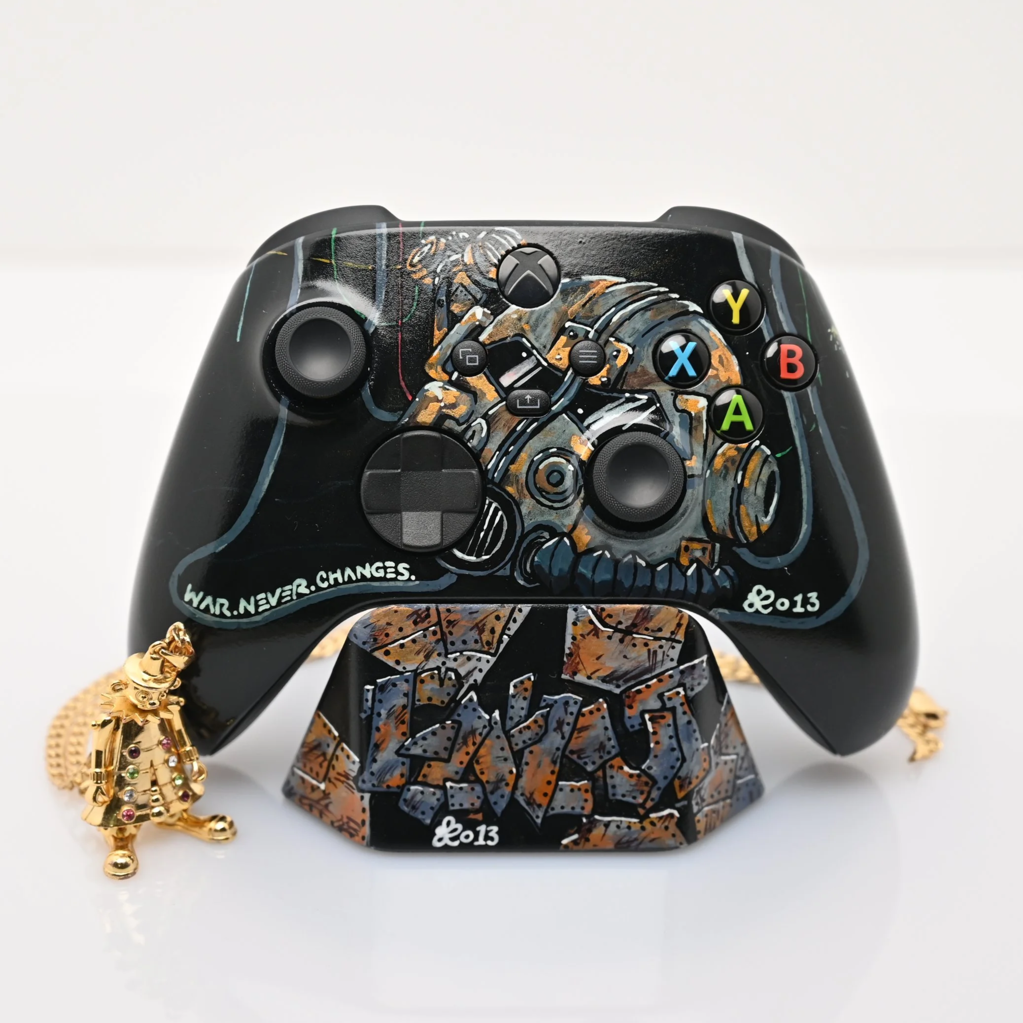 Decorative gaming controller art piece with graffiti-style design, featuring the quote 'WAR. NEVER. CHANGES.' and root-like pattern, displayed on a stand with a small charm hanging from the side.