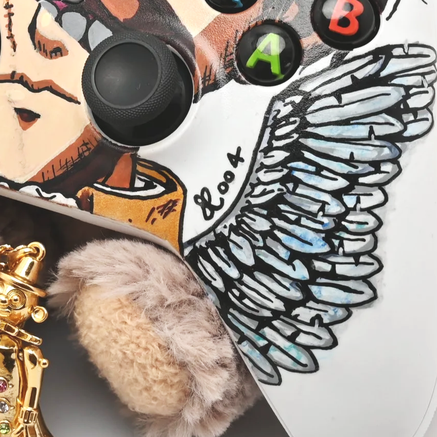Close-up of a decorated gaming controller with a cartoon face, featuring colorful buttons labeled A, B, and an analog stick. Part of a gold jewelry piece and fluffy beige object are also visible.