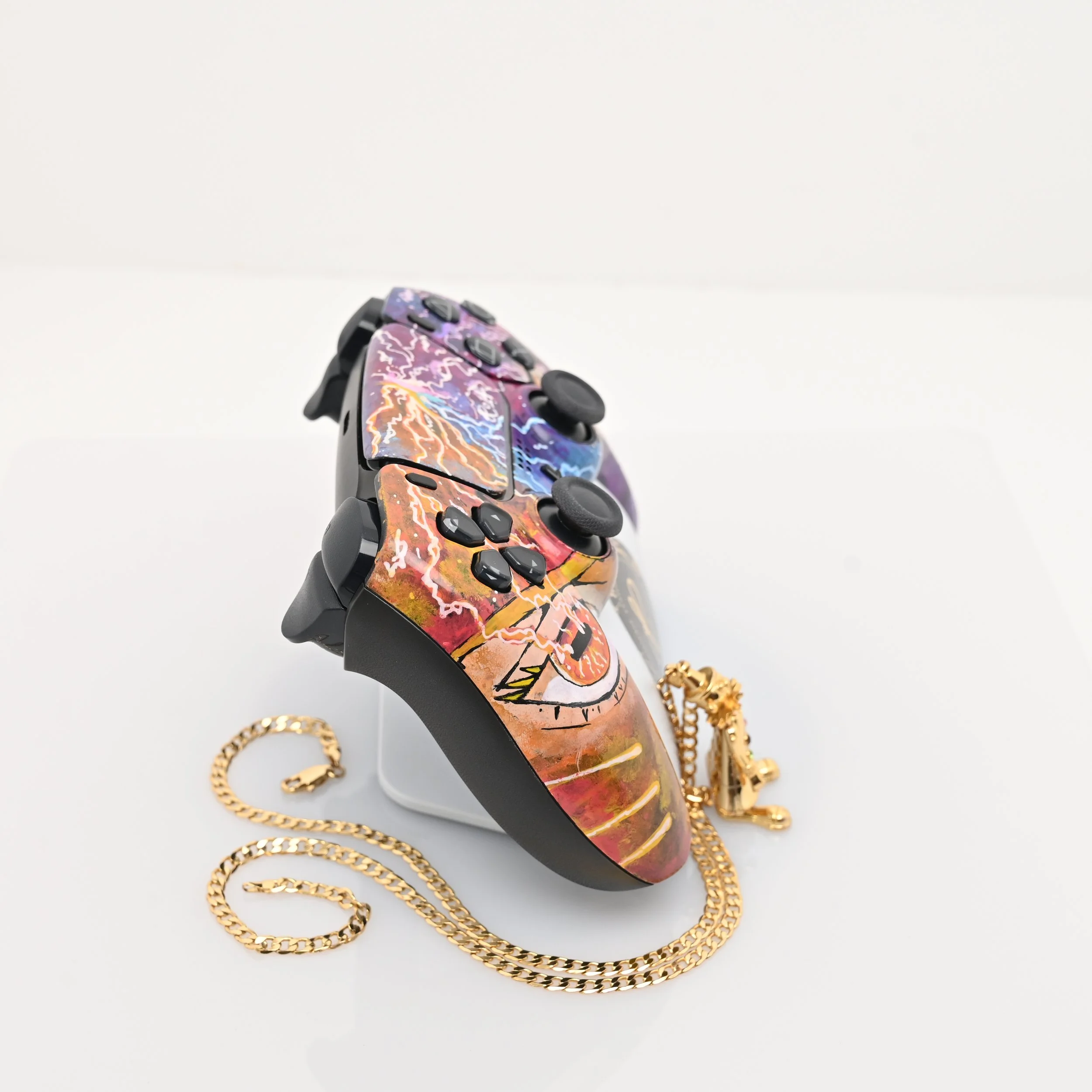 A colorful video game controller with a lightning and skull design, placed on a white surface with a gold chain necklace nearby.