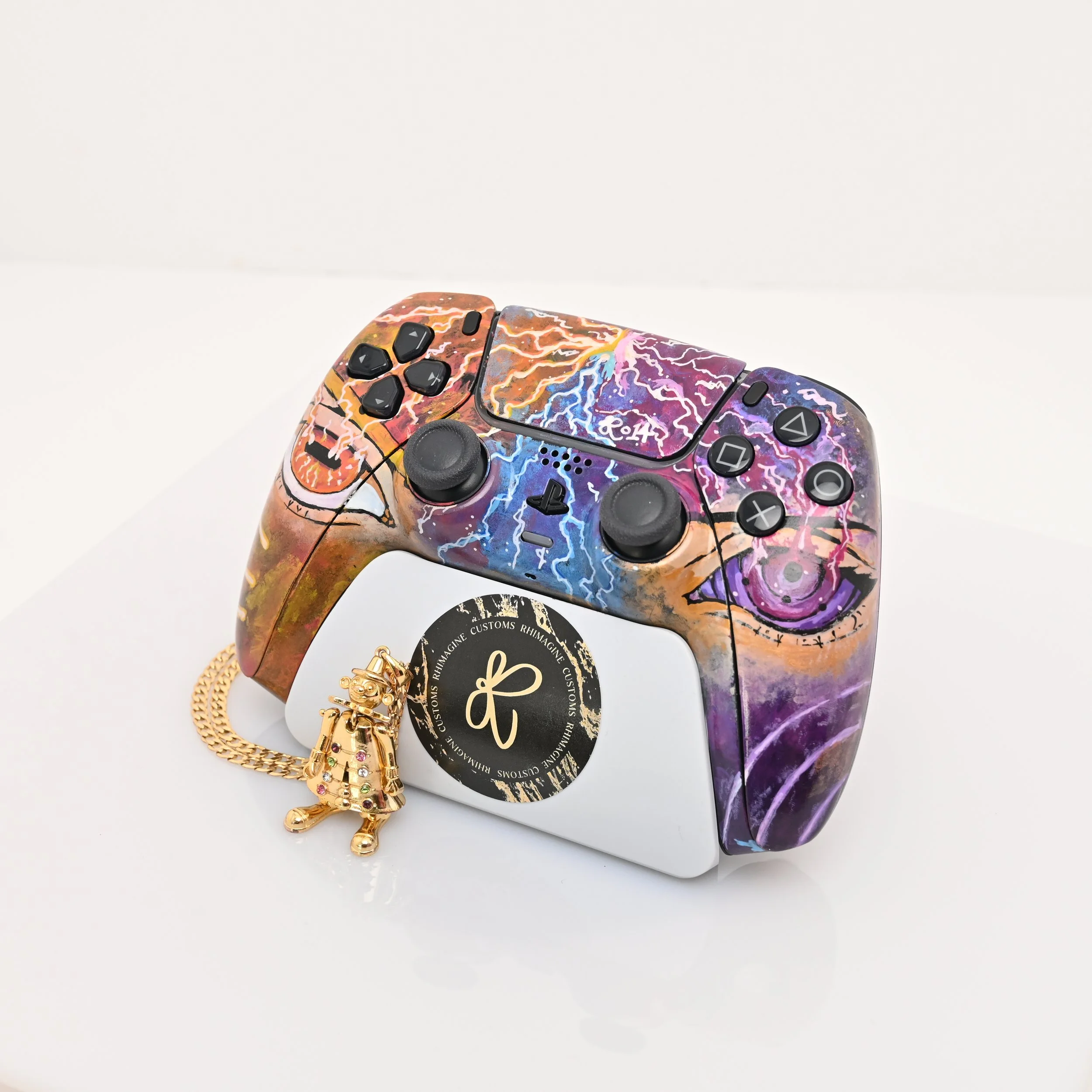 A decorated PlayStation controller with a lightning and cloud design, placed on a white surface, with a gold chain and charm in front.