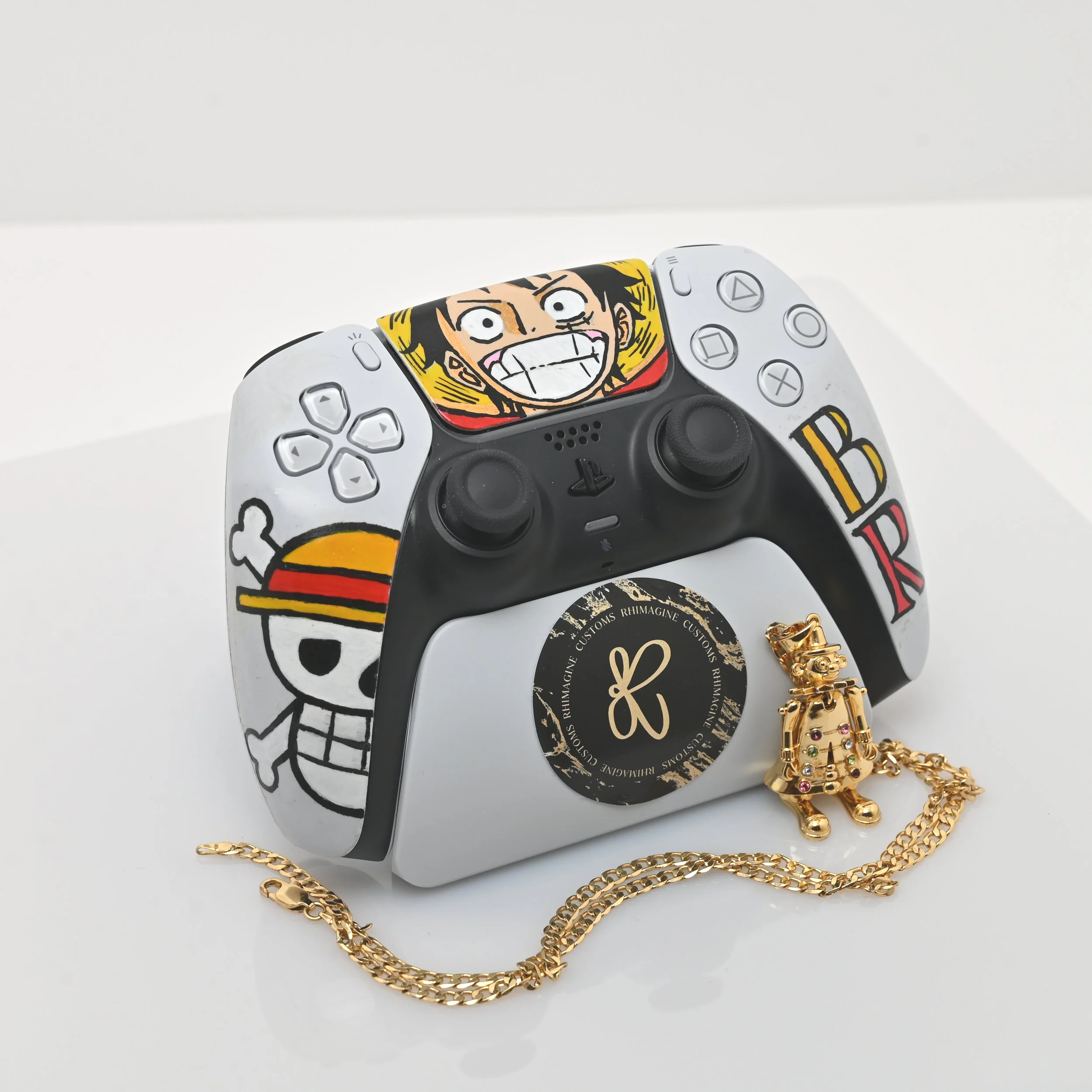 A customized PlayStation controller decorated with anime and cartoon characters and a gold chain with a pendant in the shape of a character.