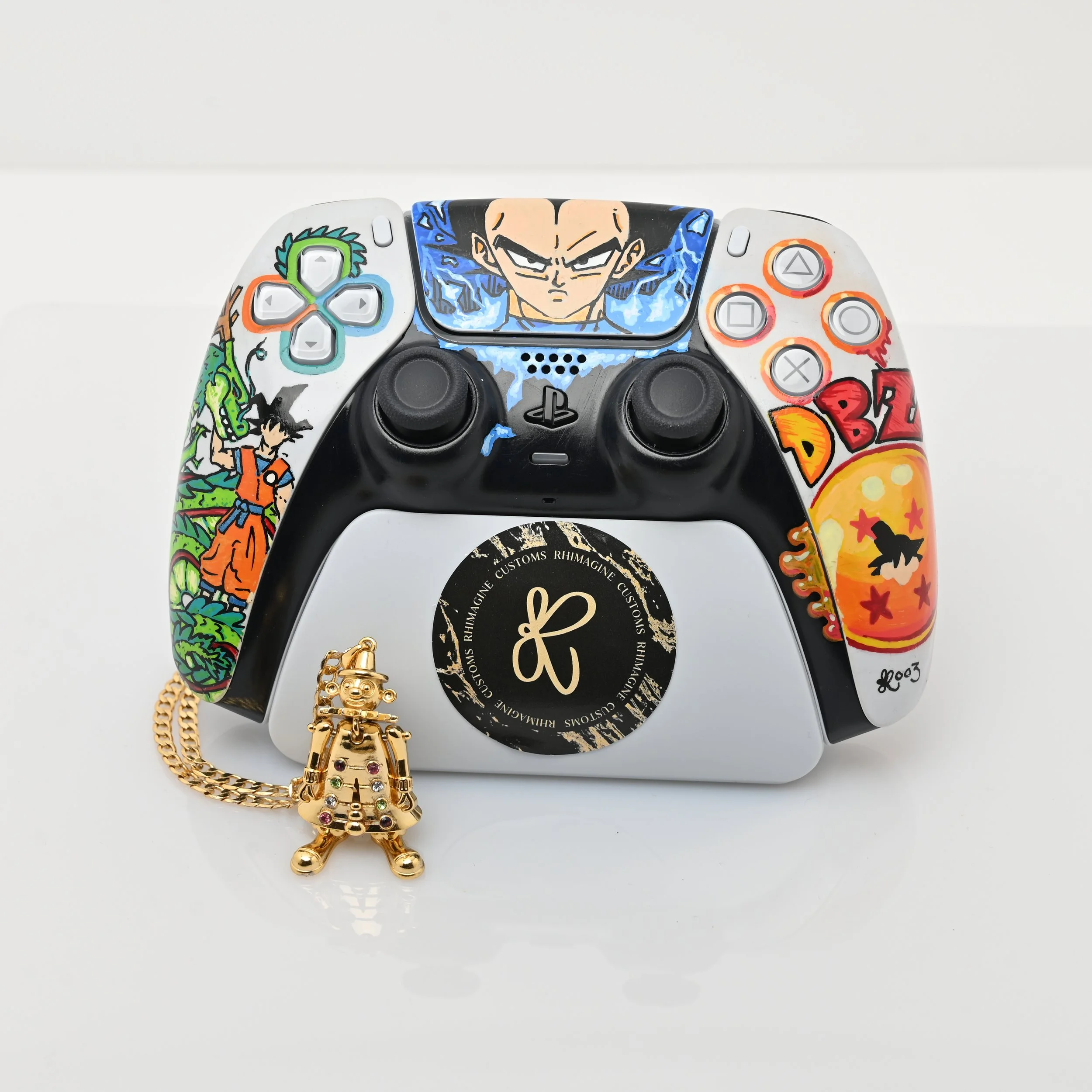 Decorated PlayStation controller with Dragon Ball Z artwork and a gold charm in front of it.