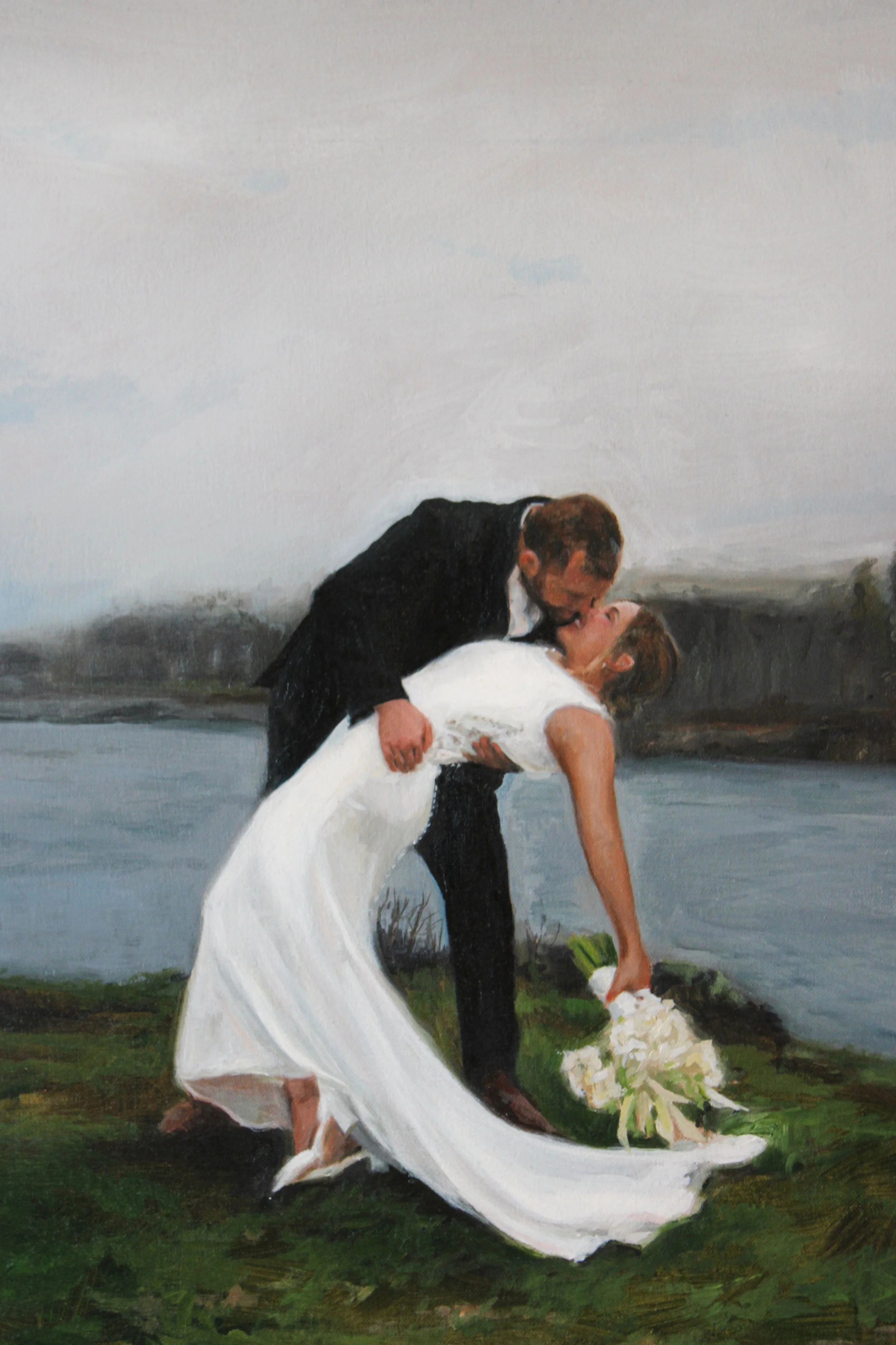 A couple is dancing outdoors by a body of water, with the woman in a white dress and the man in a black suit.