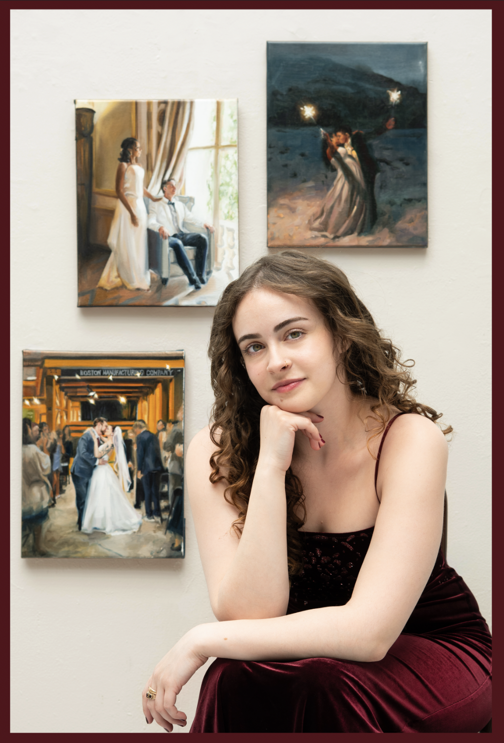Artist isabel couceiro sits in a red velvet dress with her head in her hands smiling in front of 3 wedding paintings hung on a white wall behind her.