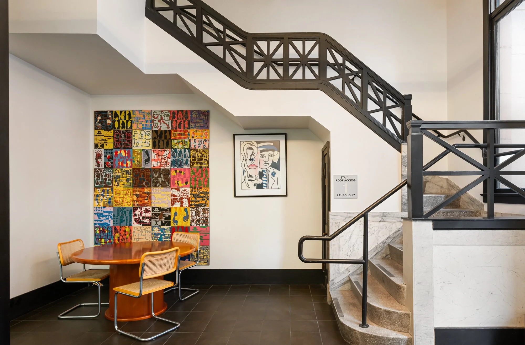 A modern interior space with a staircase, colorful artwork on the wall, and a round wooden table with four chairs.
