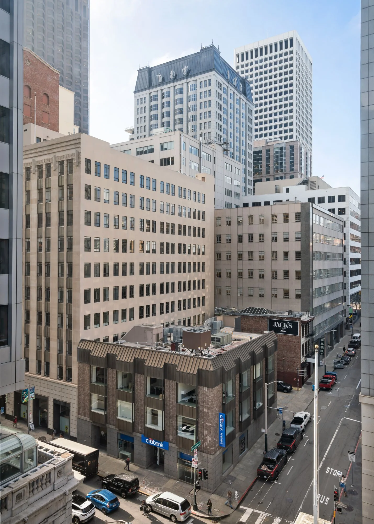 View of a city street with tall buildings, including a Citibank branch on the corner, cars parked along the street, and pedestrians walking.