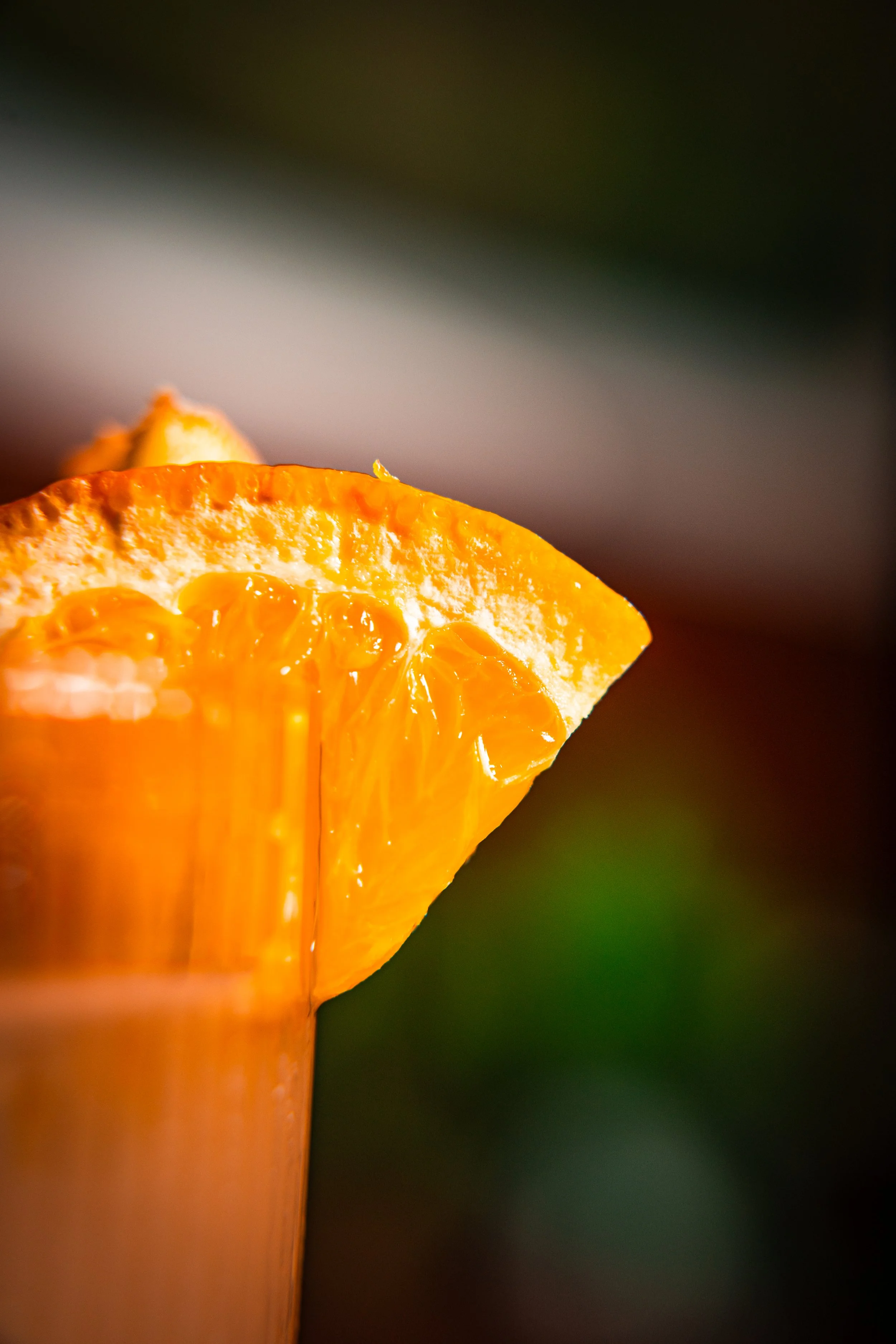 Close-up of a fresh orange wedge with a blurred dark green background.