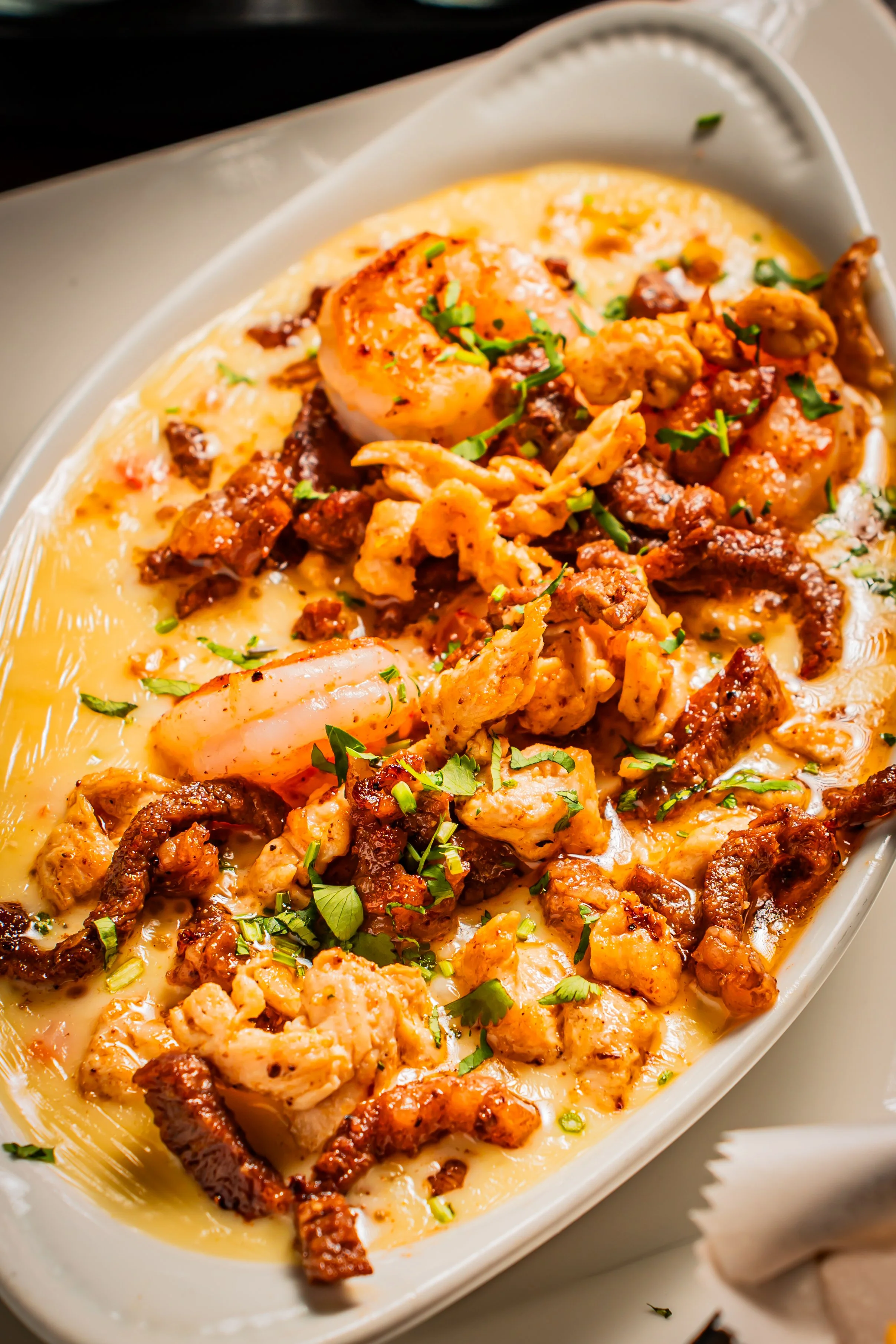 Seafood platter with shrimp, lobster, and chopped herbs in a creamy sauce in a white dish.