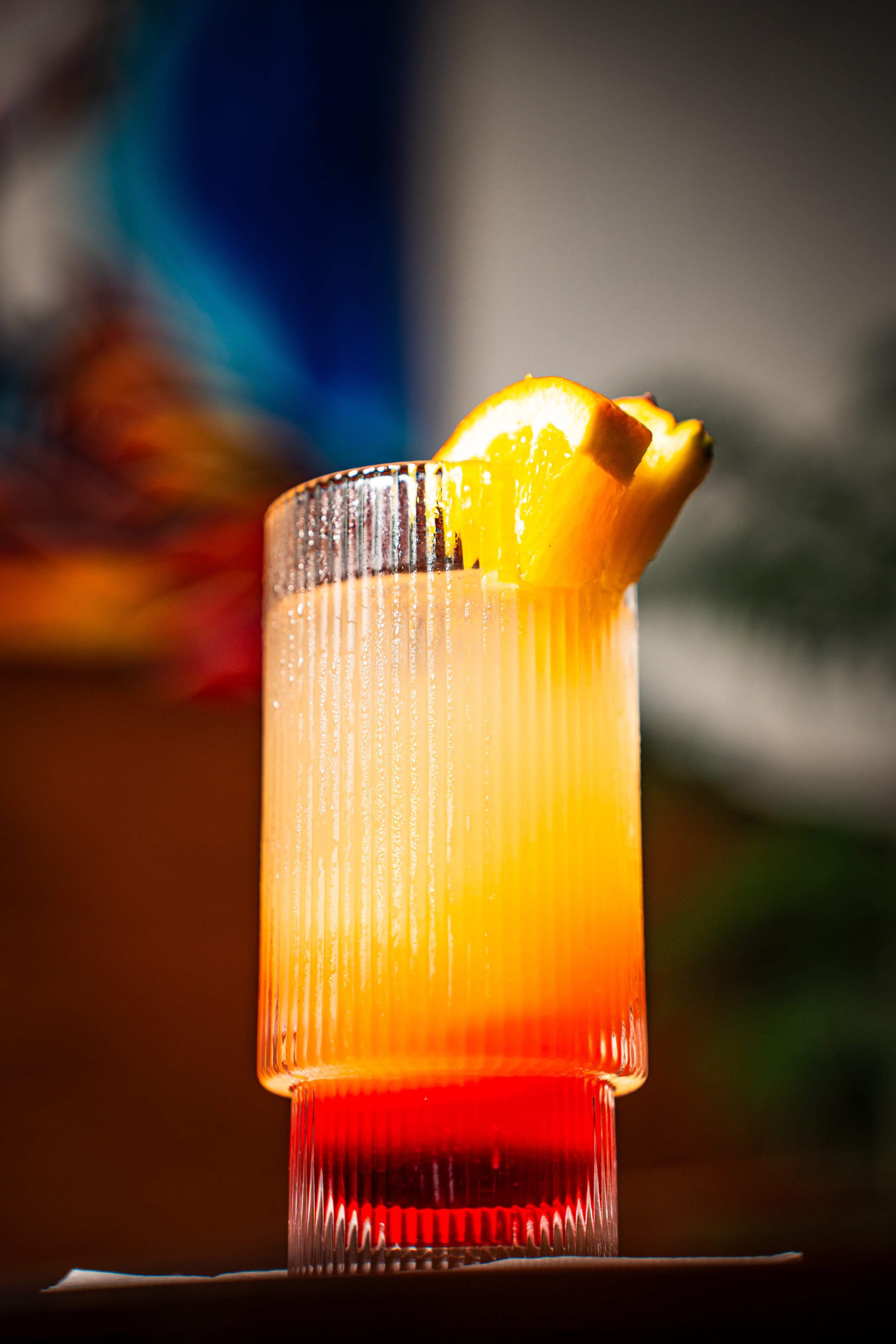 A colorful layered cocktail in a textured glass garnished with a slice of lemon.