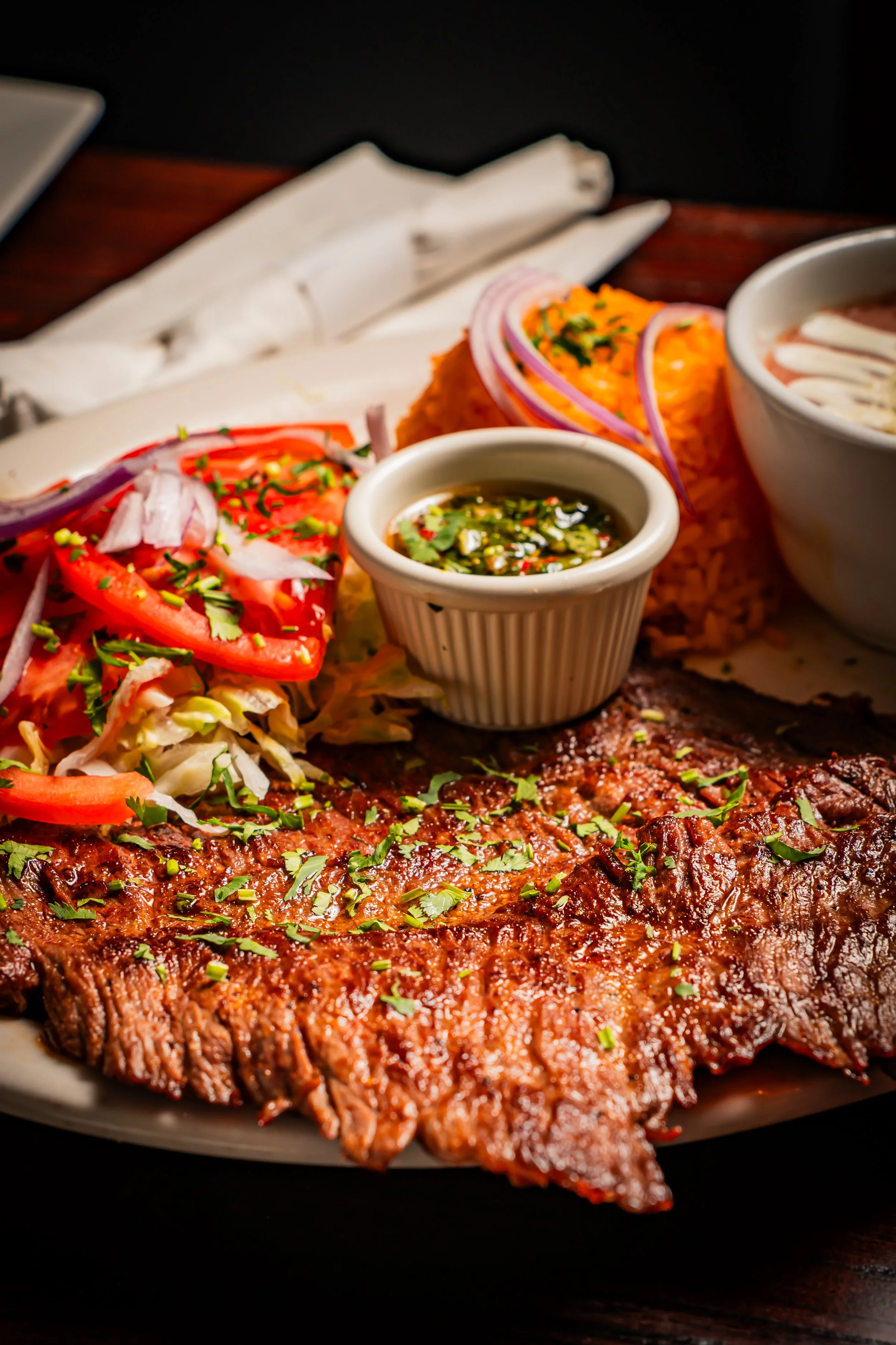 A plate of grilled meat served with salad, rice, and sauces at a restaurant.
