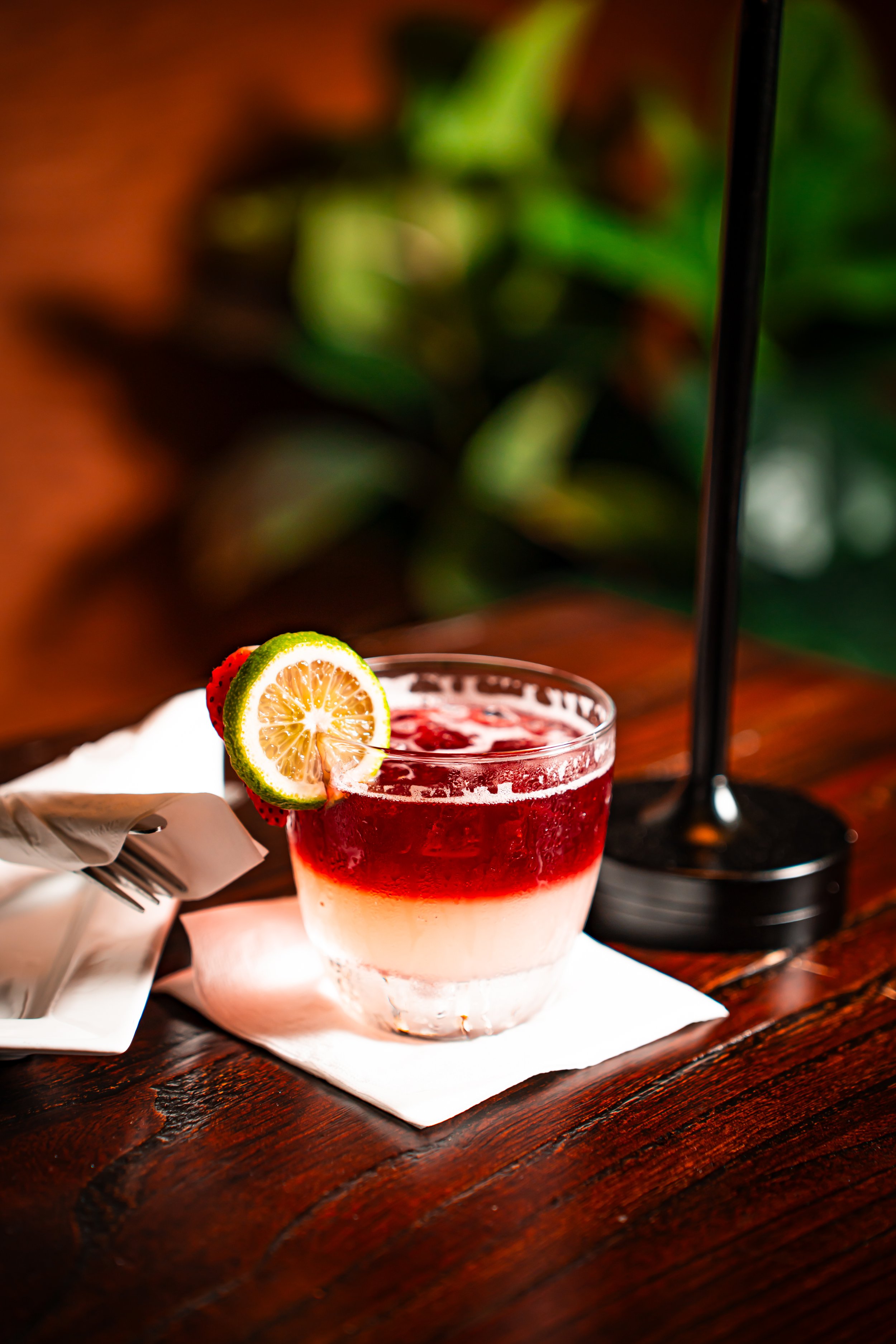 Layered cocktail with lemon and strawberry garnish on a wooden table.