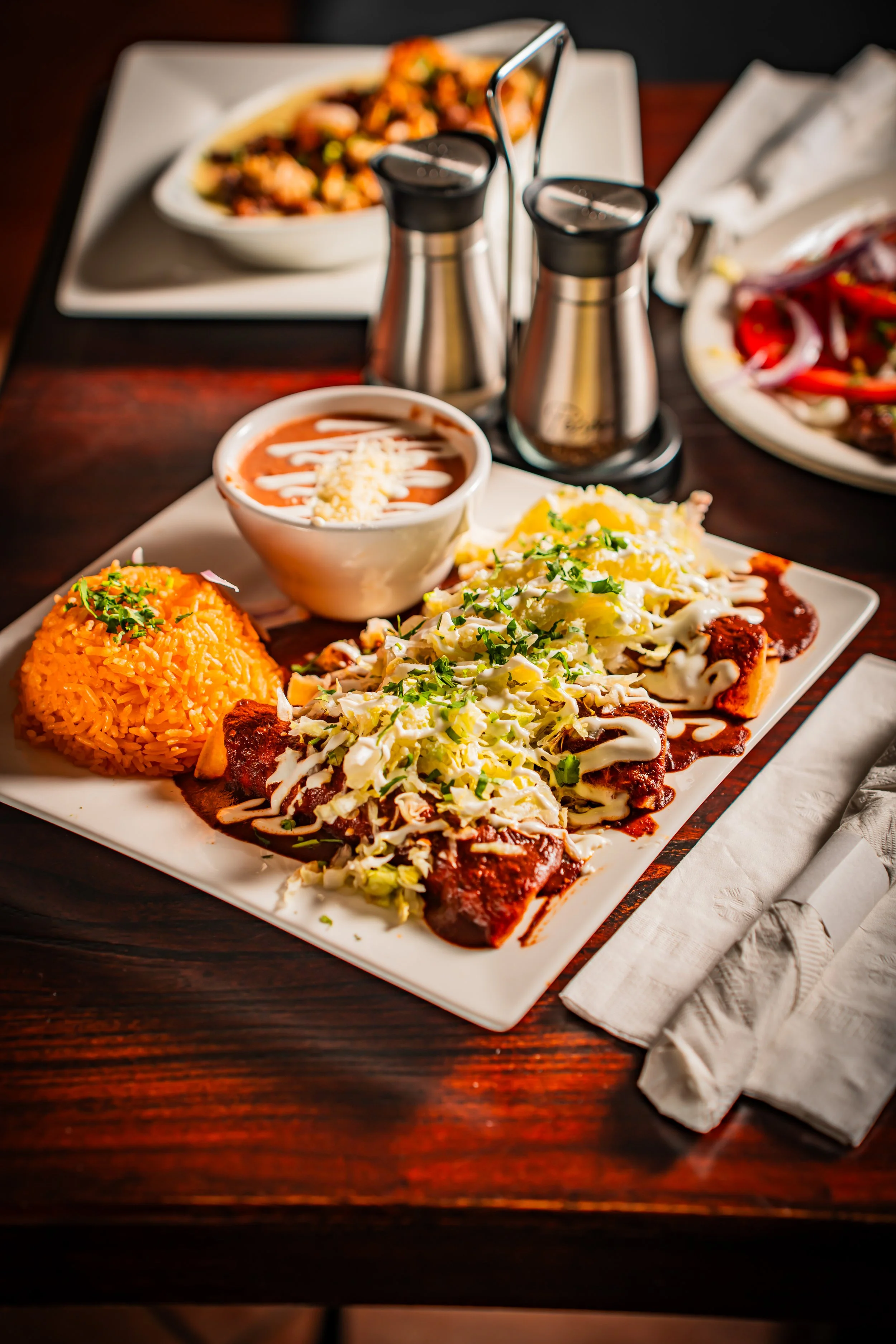 Plate of Mexican food with rice, beef and cabbage, a bowl of soup, and a side of salsa with tortilla chips on a wooden table.