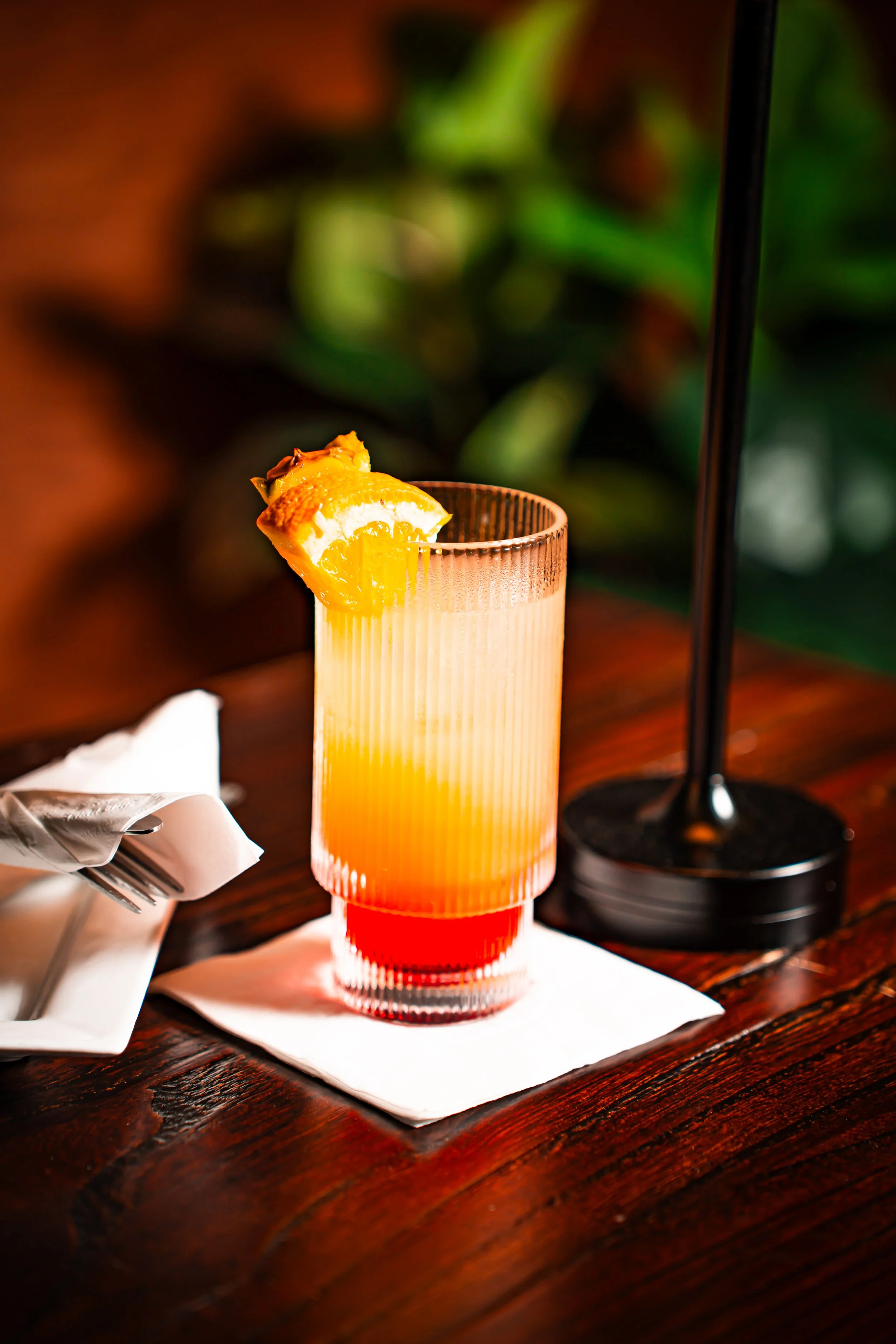 A colorful cocktail with a lemon wedge garnish on a wooden table.
