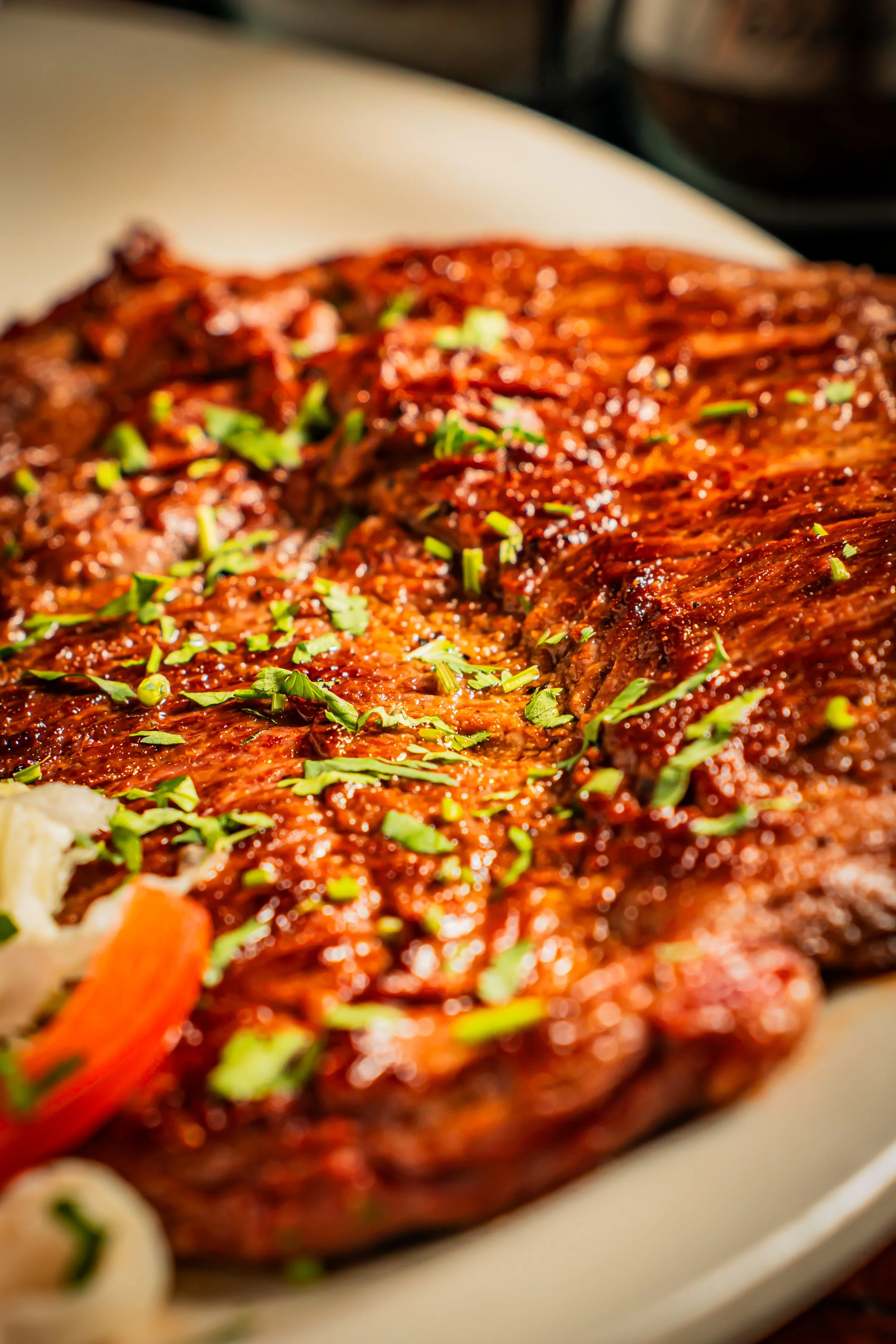 Close-up of a cooked beef brisket topped with chopped green herbs, served on a white plate.