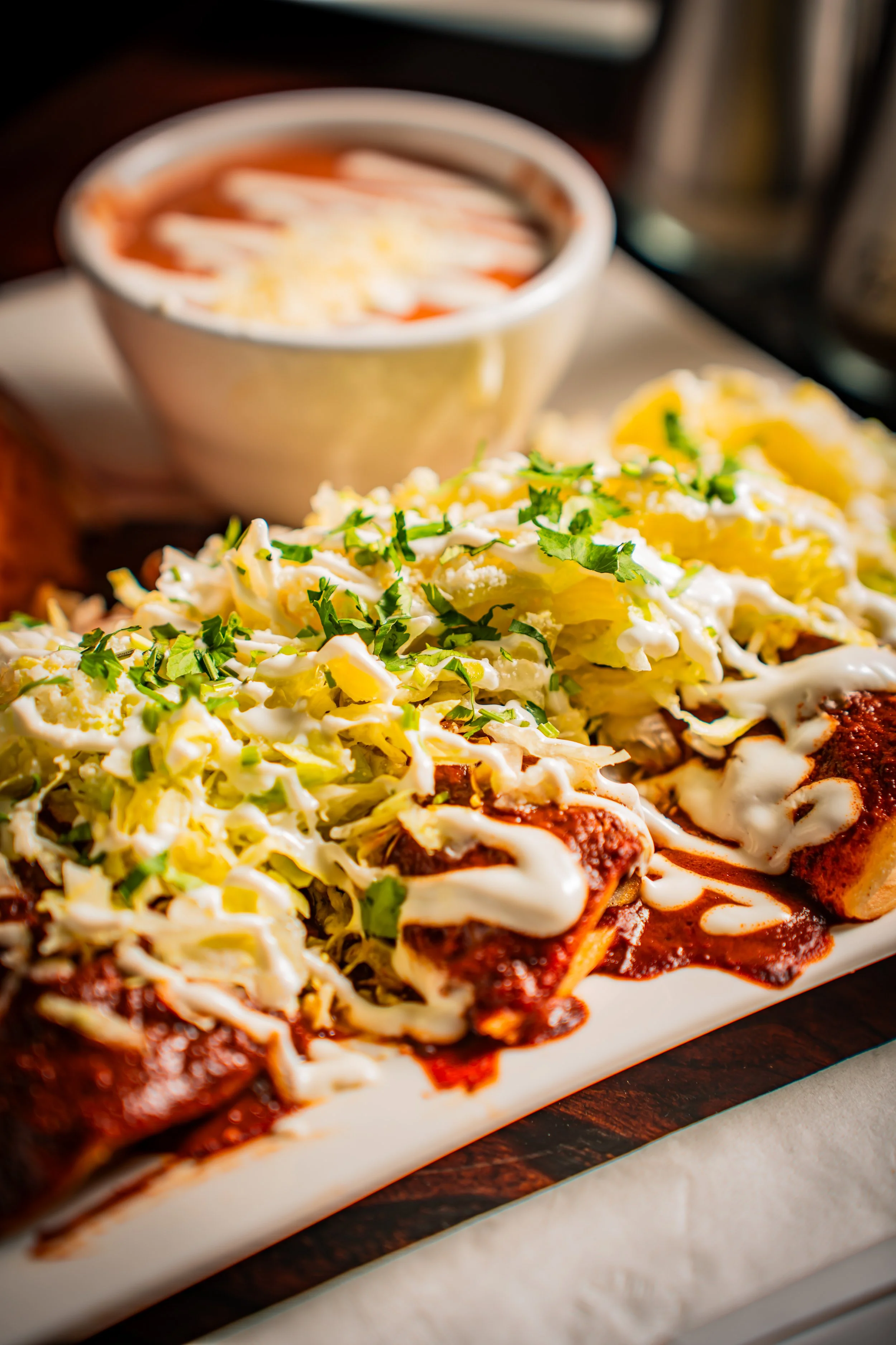 Enchiladas topped with shredded cabbage, cilantro, and sour cream, served with a side of red sauce.
