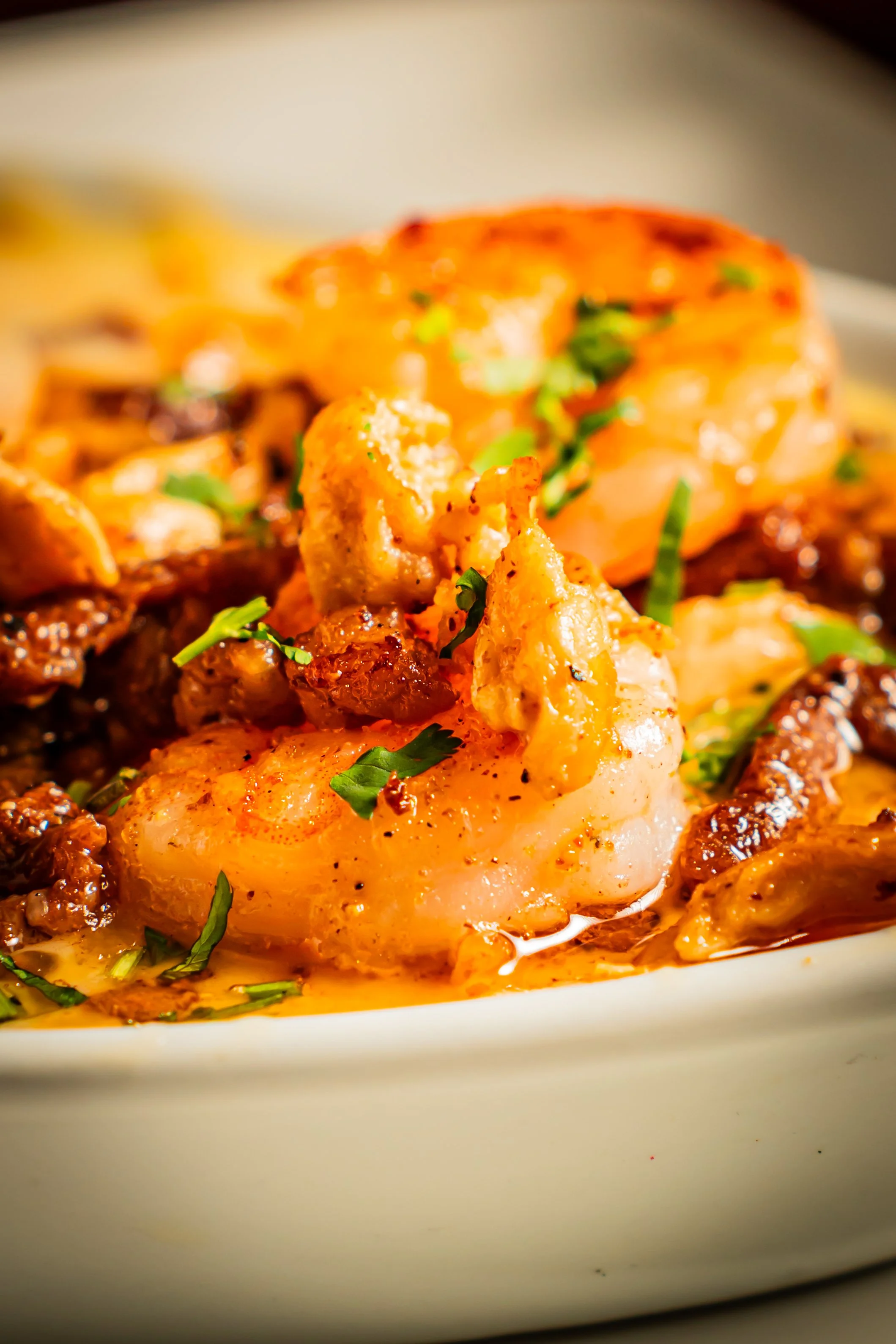 Close-up of shrimp and shrimp tails garnished with green herbs on a plate with sauce.