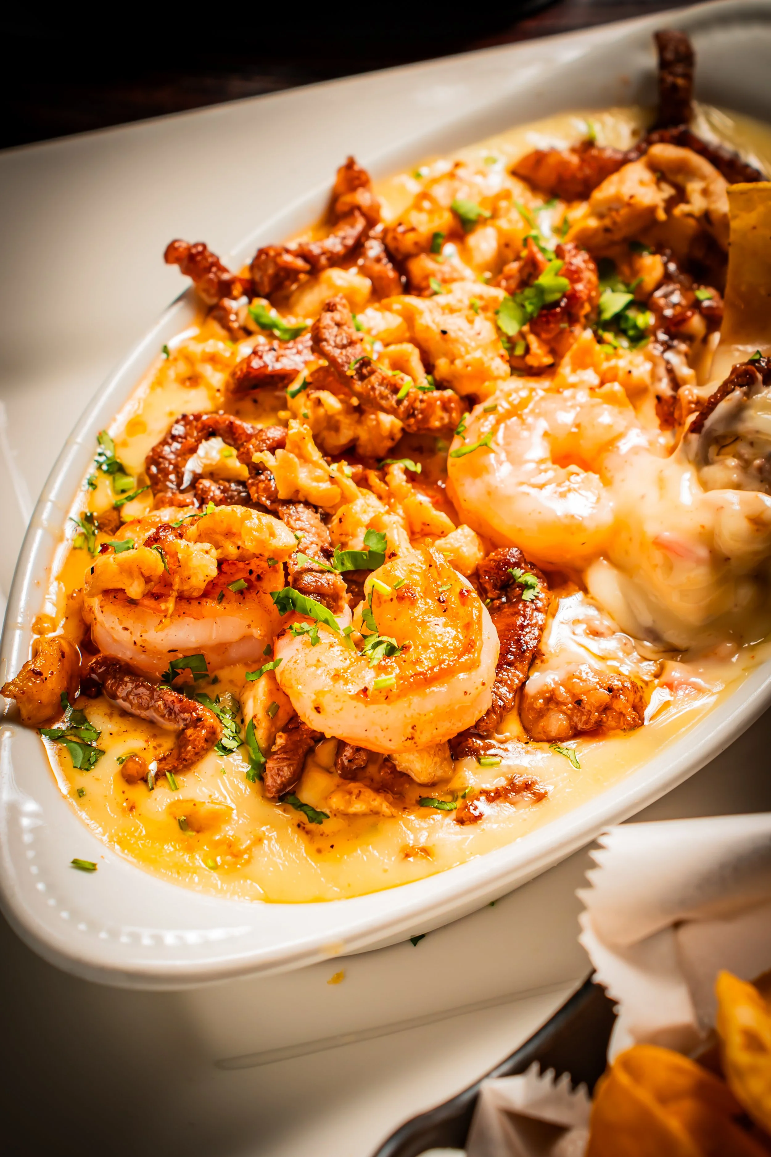 Seafood dish with shrimp, fried chicken, and garnished with chopped herbs in a creamy sauce.